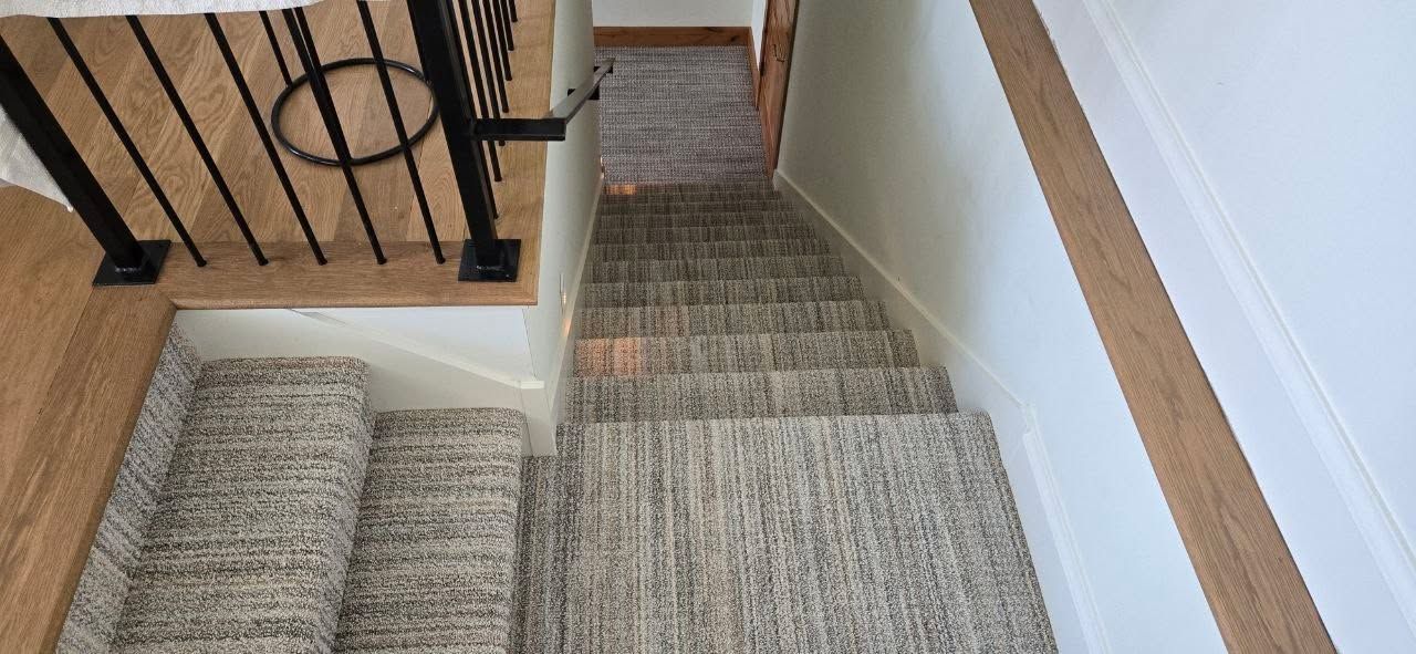 Carpet-covered staircase with matching hallway runner in gray tones and black metal railing.