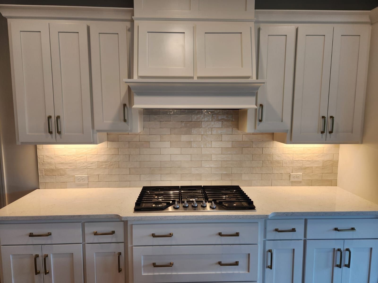Kitchen with white subway tile backsplash and under-cabinet lighting above gas cooktop.
