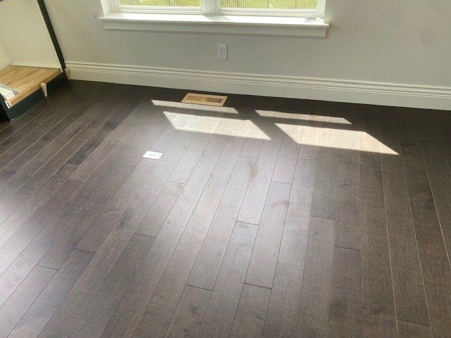 Dark hardwood plank flooring installed in a bedroom with natural light from a window.