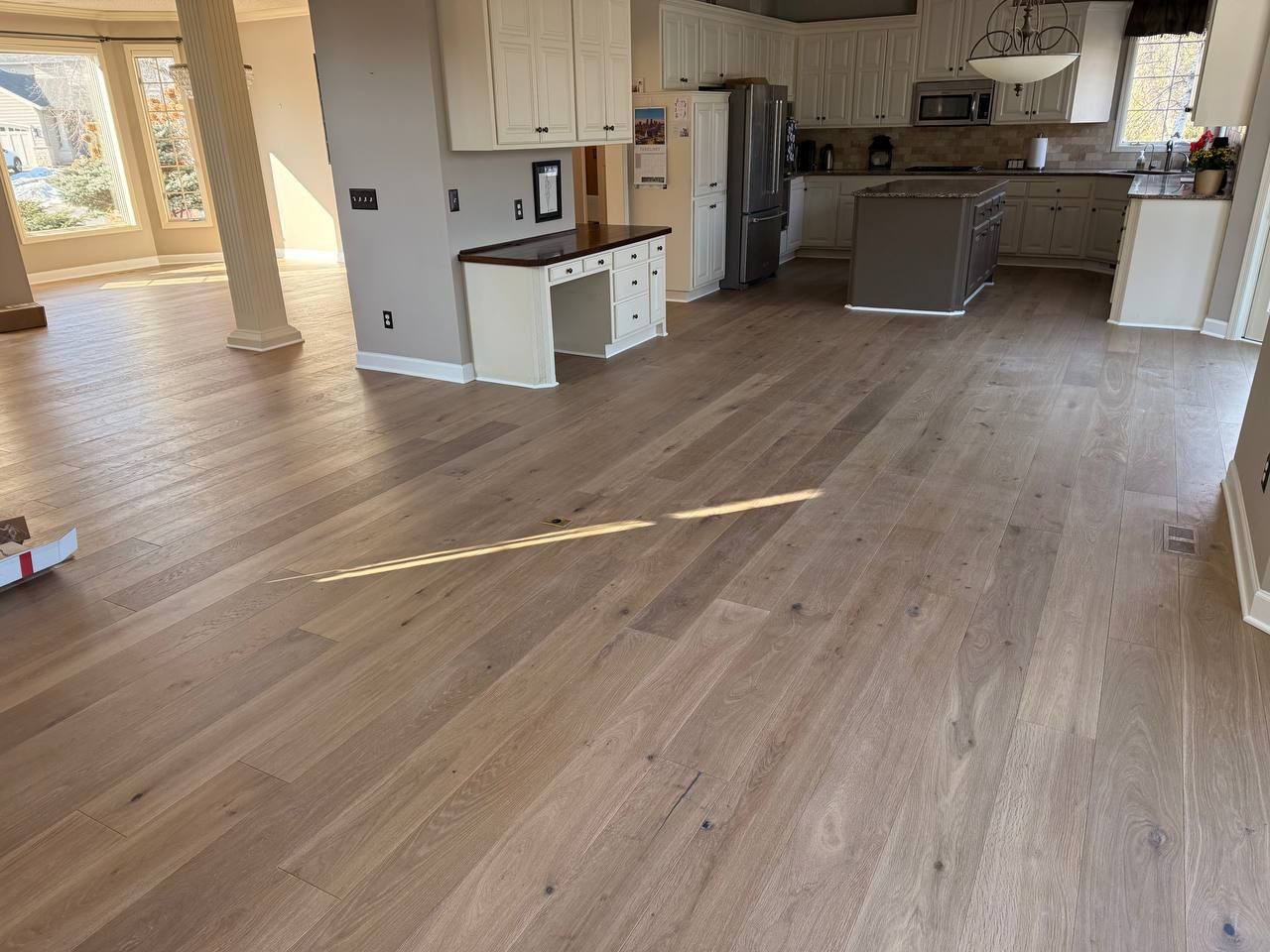 Kitchen with medium-toned hardwood plank flooring, white cabinetry, dark countertops, and island.