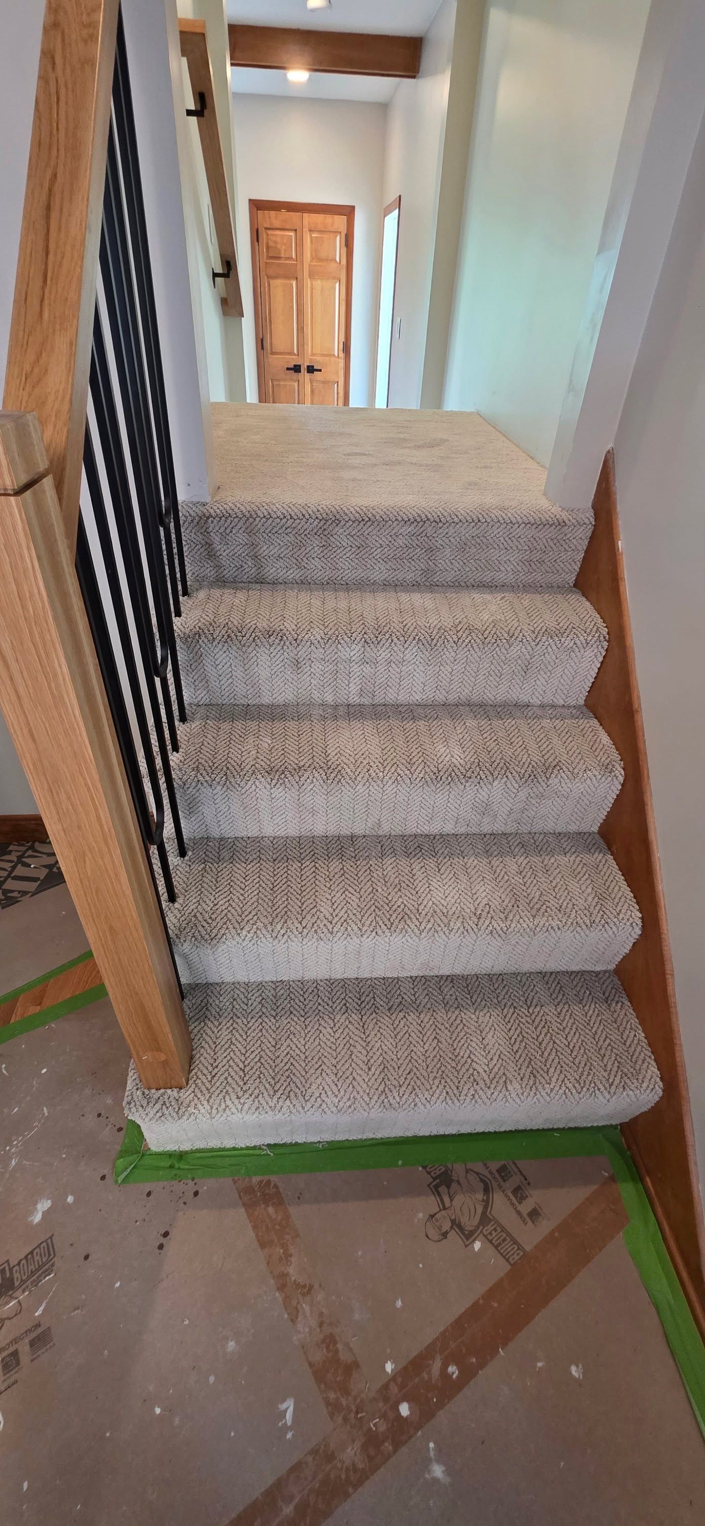 Newly installed gray and white striped carpet on residential staircase with wooden railings.