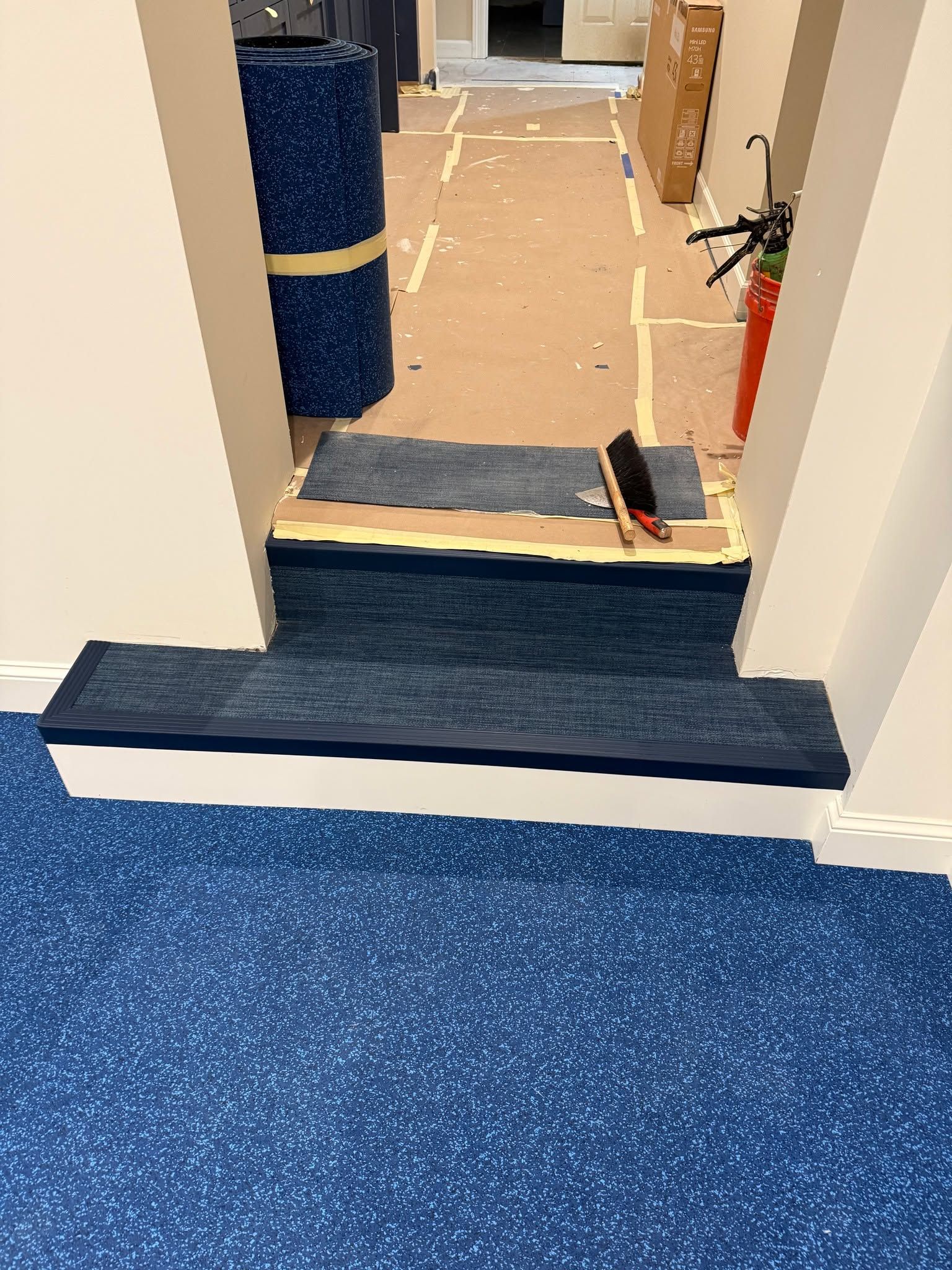 LVP flooring installation in entryway showing dark plank material with existing blue carpet and protective coverings.