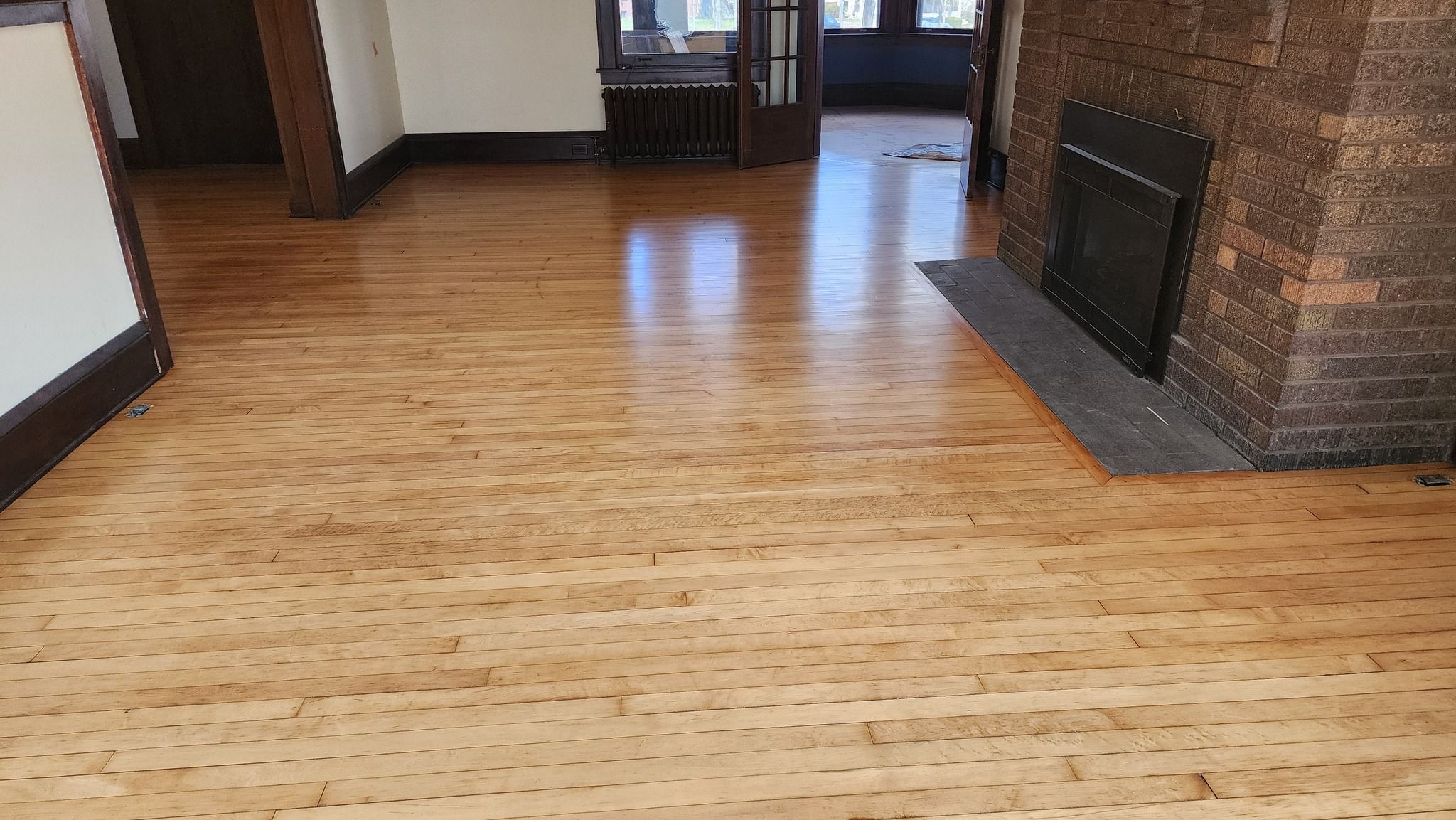 Refinished maple hardwood plank flooring in a living room with a brick fireplace and dark wood trim.