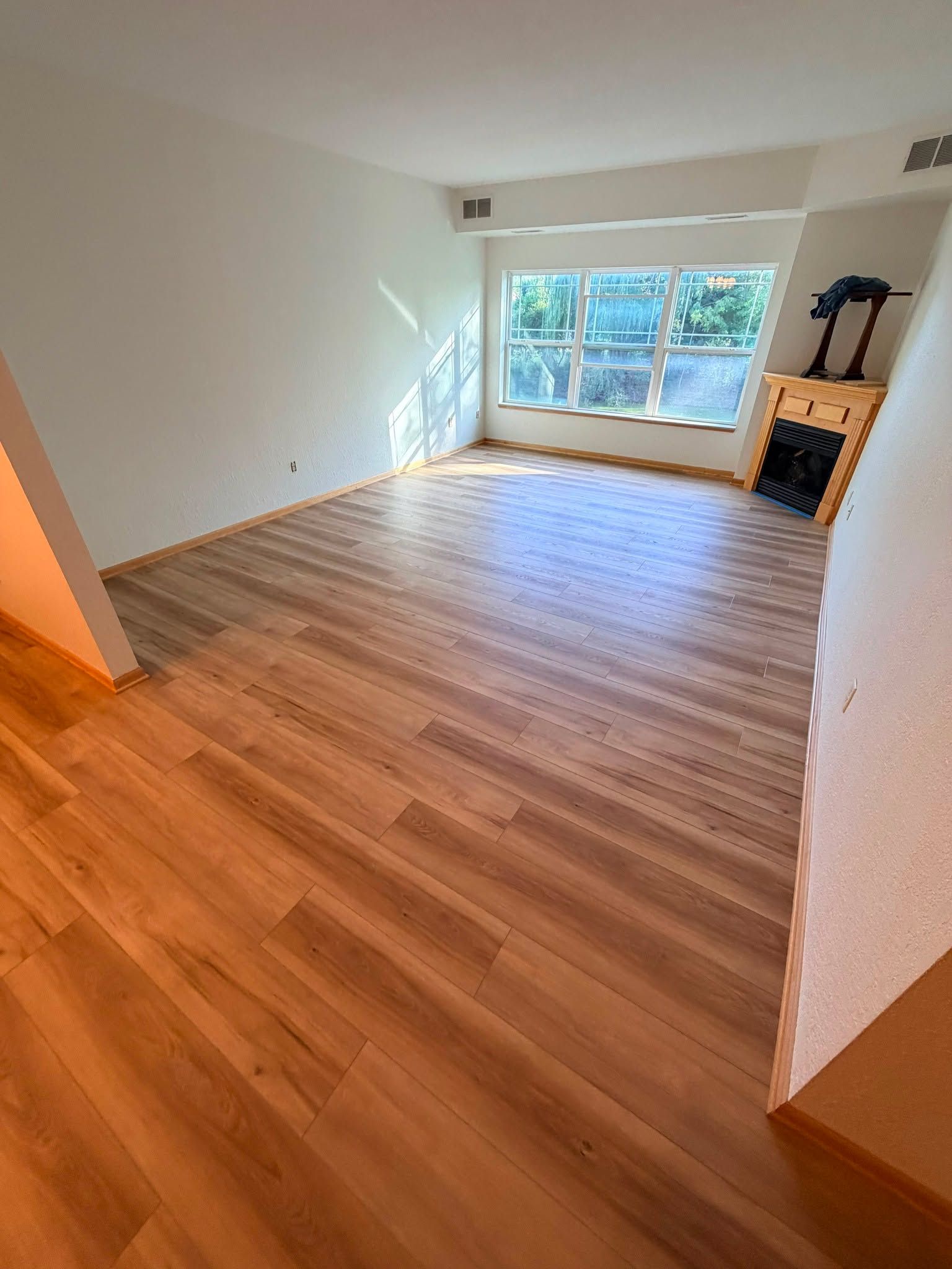 Newly installed medium-toned hardwood plank flooring in a bright living room with large windows.