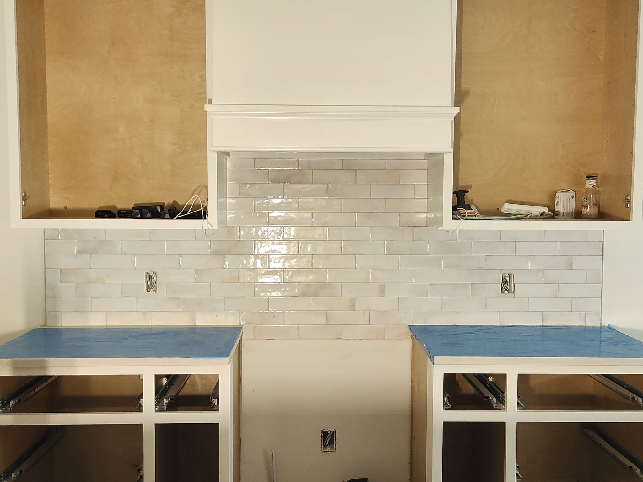White subway tile backsplash behind kitchen counter with range hood and open cabinetry on either side.