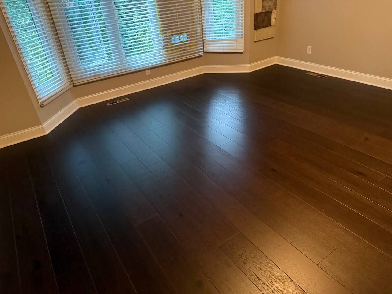Dark hardwood plank flooring in a living room with curved walls and bay windows.