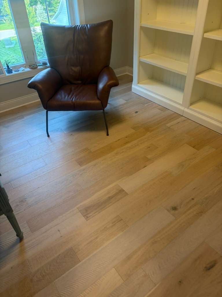 Light tan hardwood plank flooring installed in a living room with built-in shelving and large windows.