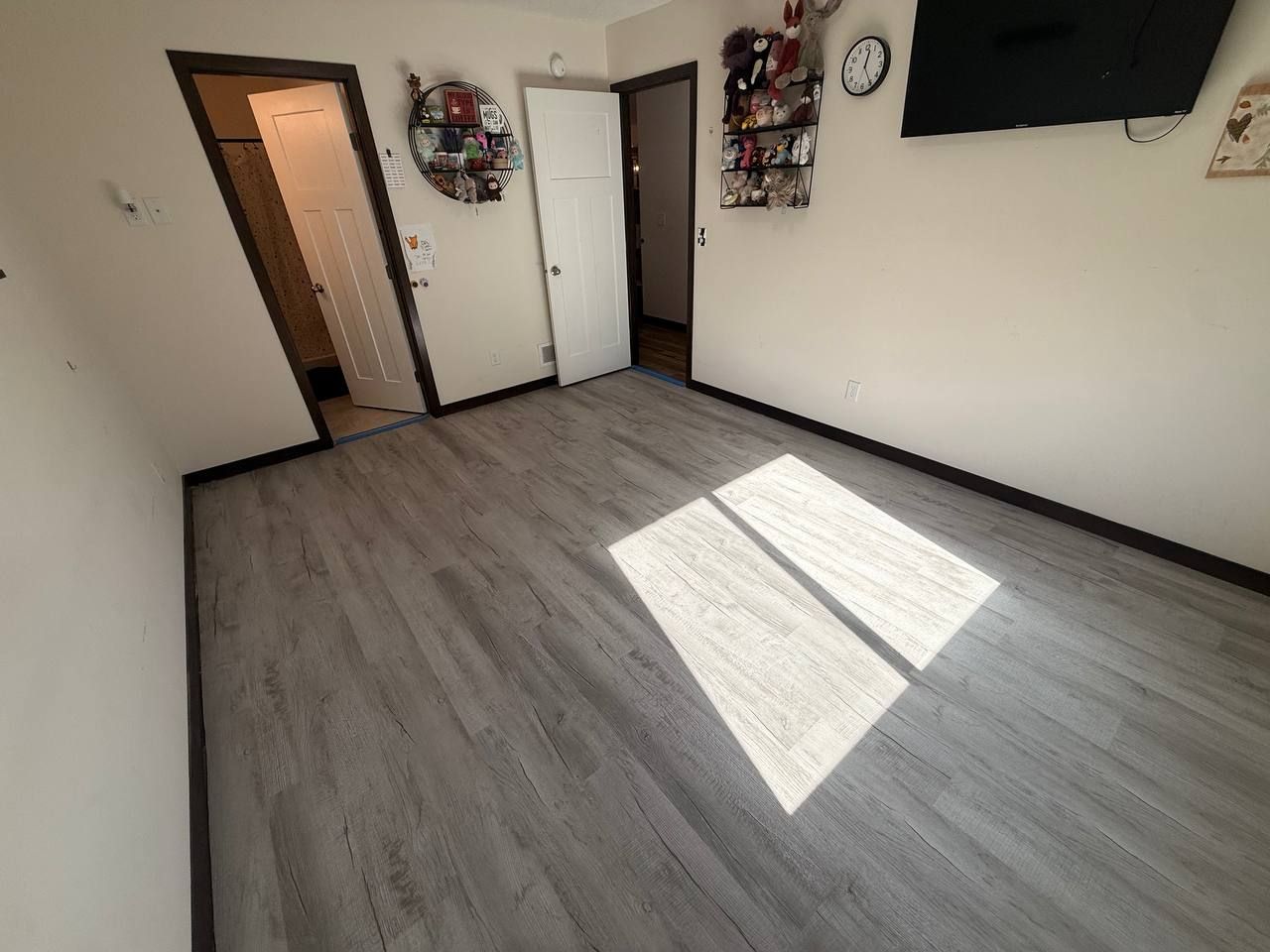 Gray plank LVP flooring installed in a bedroom with white walls and multiple doors.
