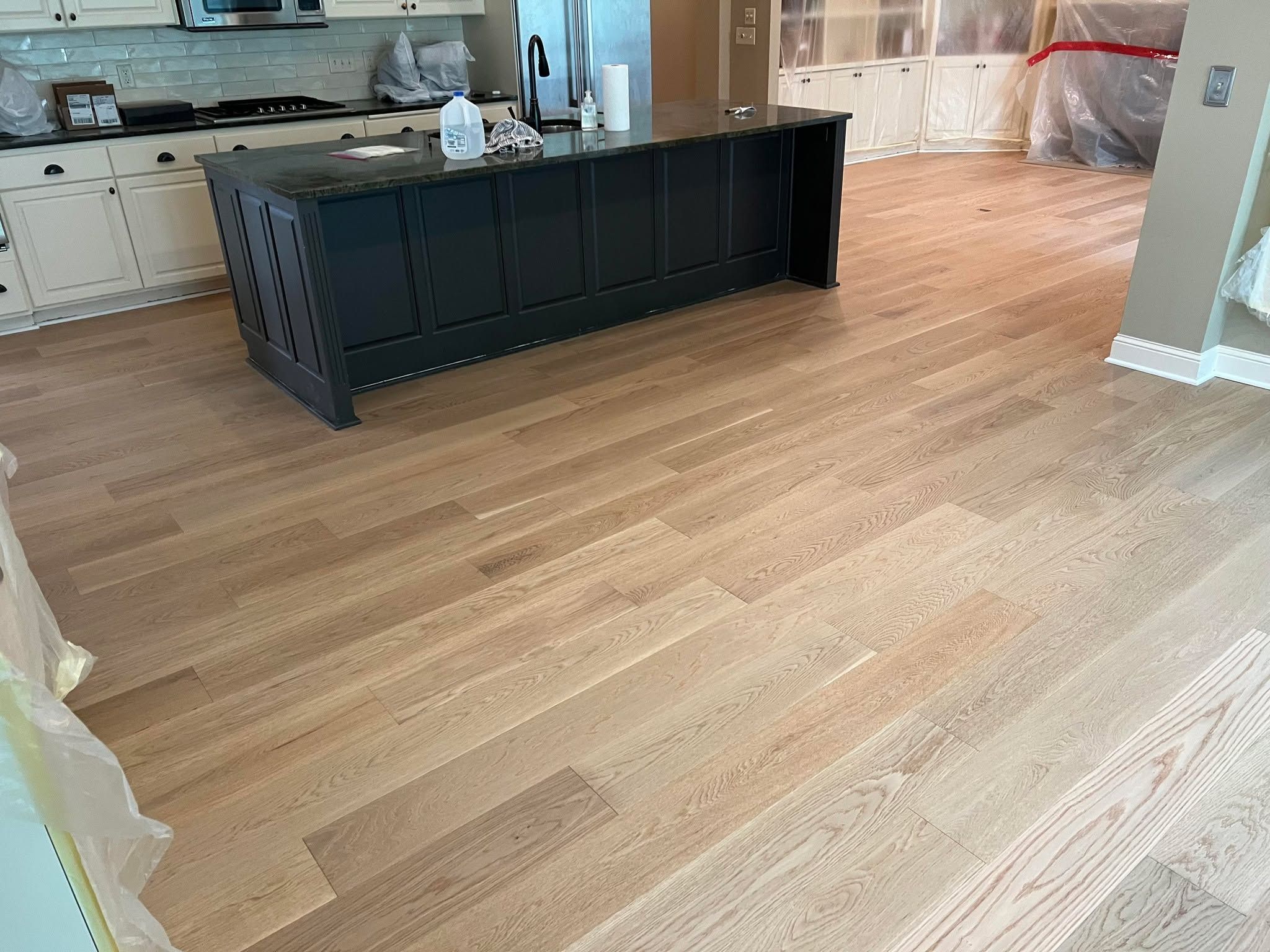 Newly installed medium-toned hardwood plank flooring in kitchen with black island and white cabinetry.