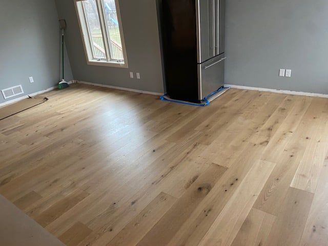Light tan hardwood plank flooring in a kitchen with appliances and large windows.
