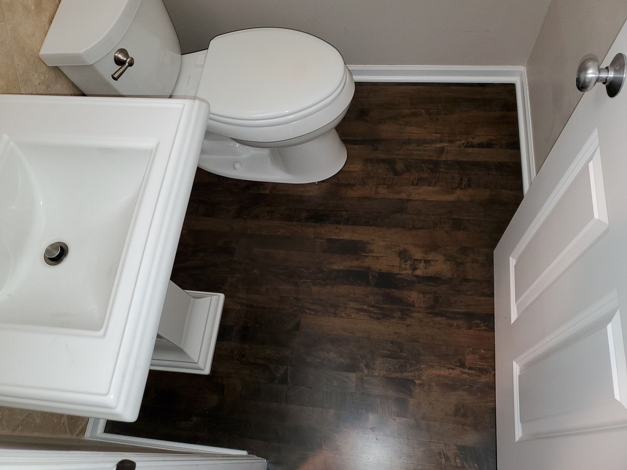 Dark hardwood plank flooring installed in a bathroom with white fixtures and trim.