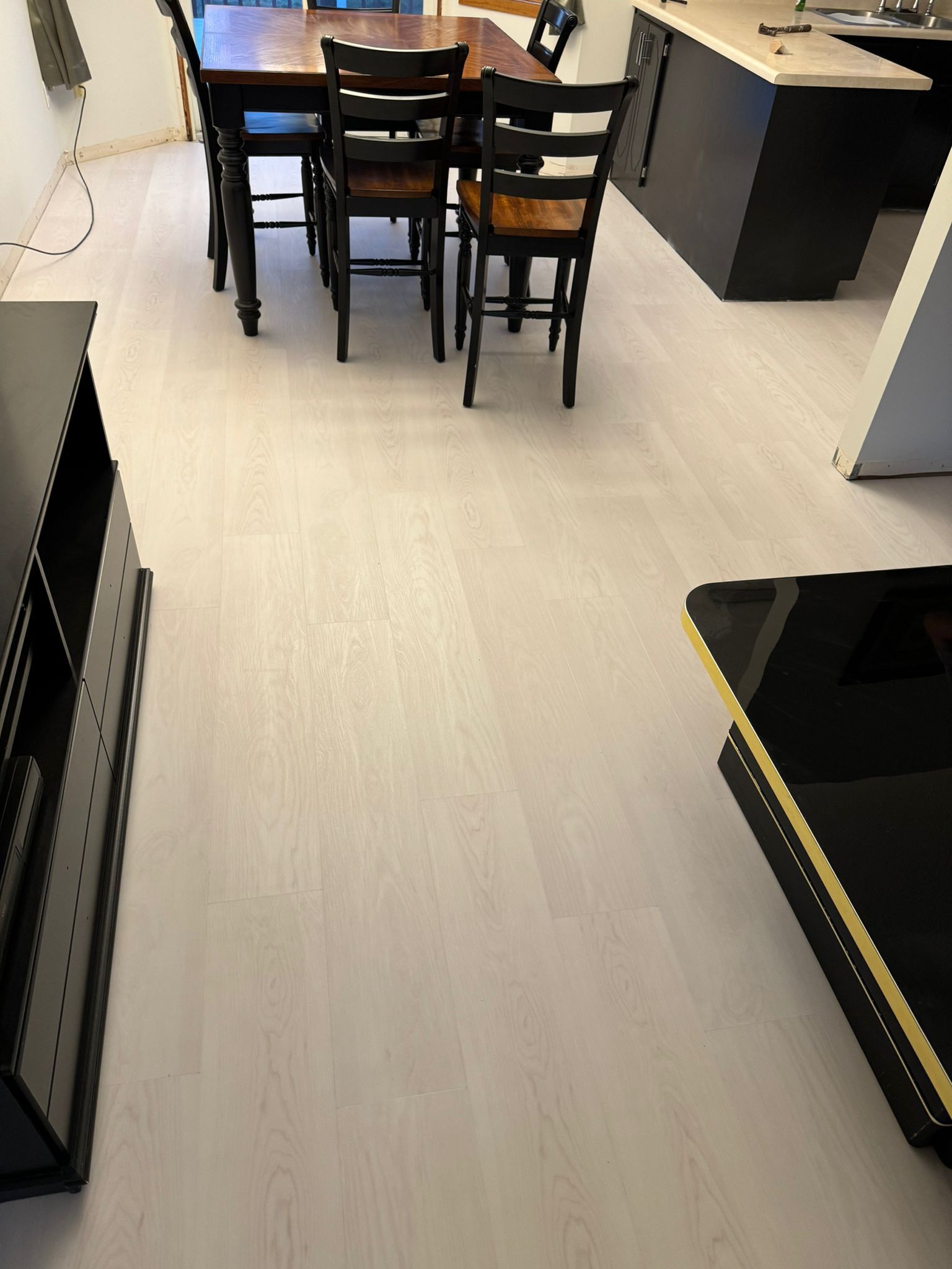 Light colored plank LVP flooring installed throughout a kitchen and dining area with black cabinets and wood dining table.