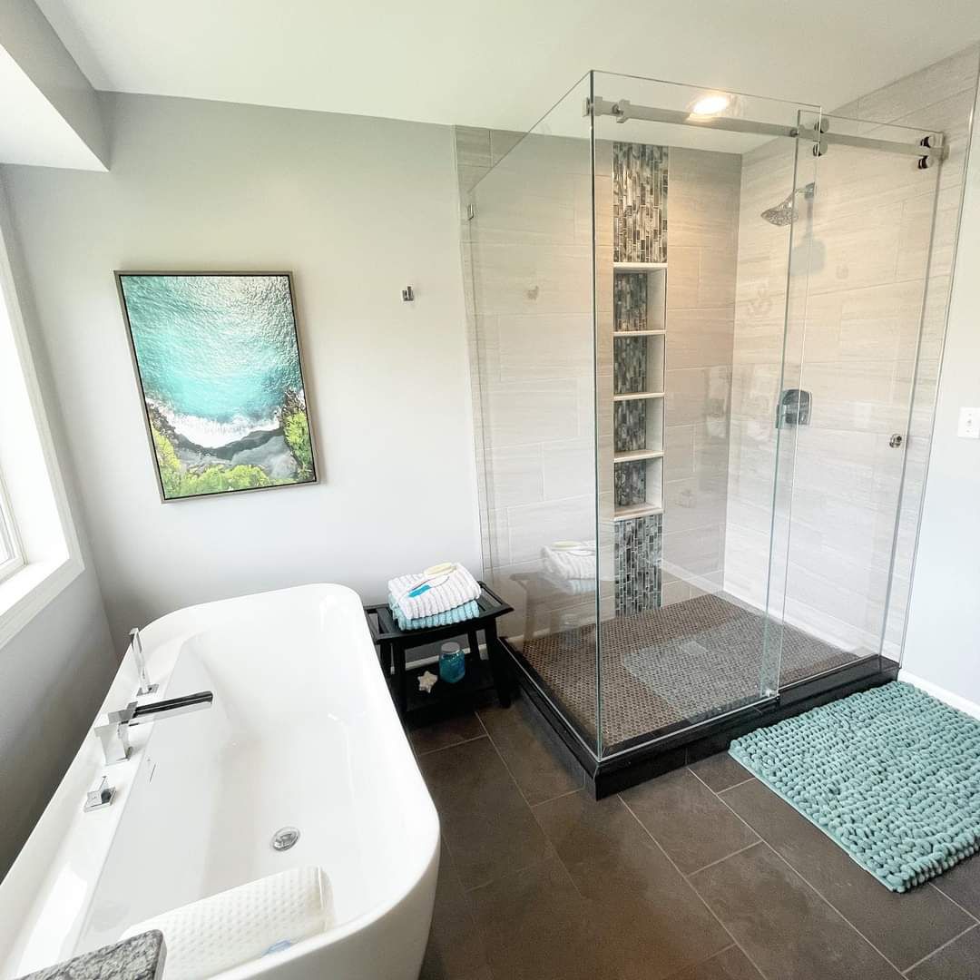 Bathroom with white subway tile walls, gray tile flooring, freestanding soaking tub, and large glass shower enclosure with mosaic accent tile.