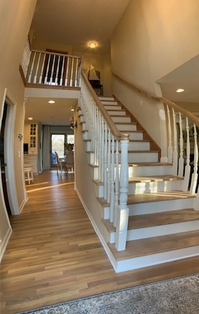 Hardwood staircase with white railings and tan and brown treads installed in an entry hallway with matching wood flooring.