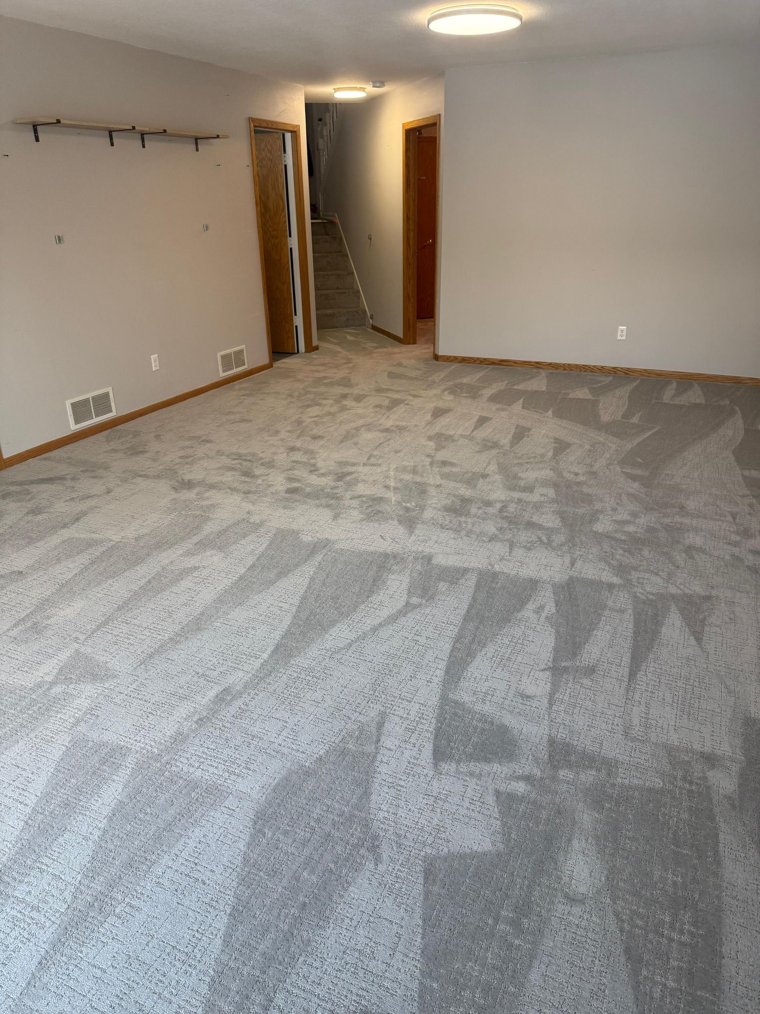 Newly installed gray and beige carpet with geometric pattern in a basement room with wood trim.