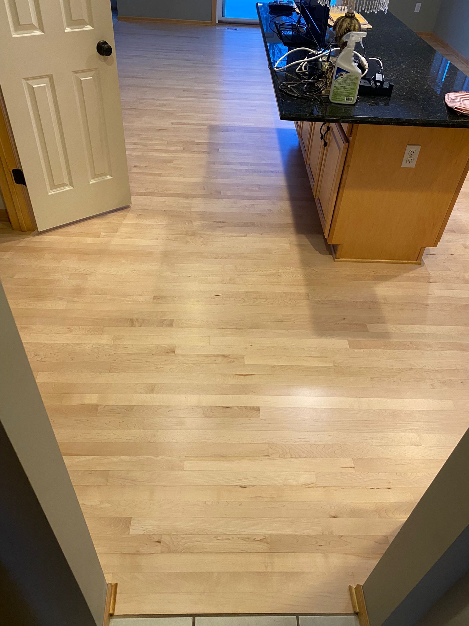 Light maple hardwood plank flooring in a kitchen with island and wooden cabinets during refinishing work.