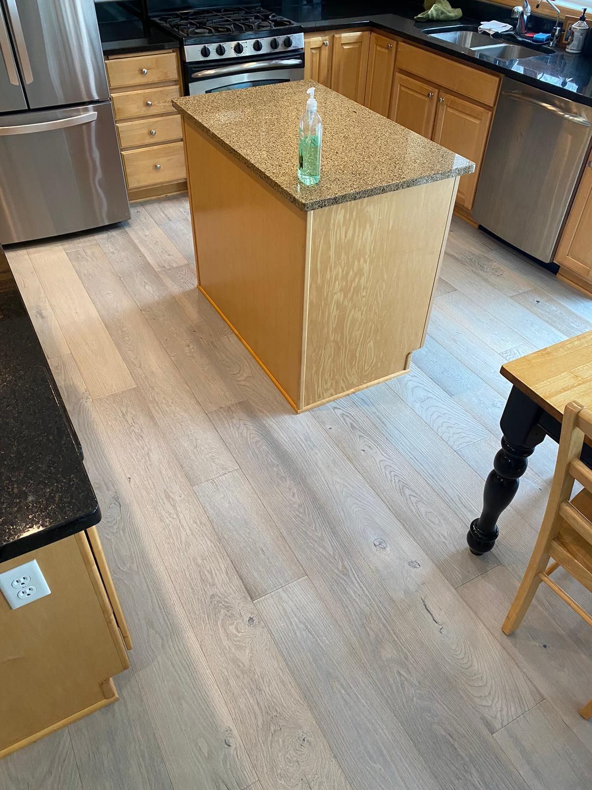 Light hardwood plank flooring installed in a kitchen with wood cabinets and island.