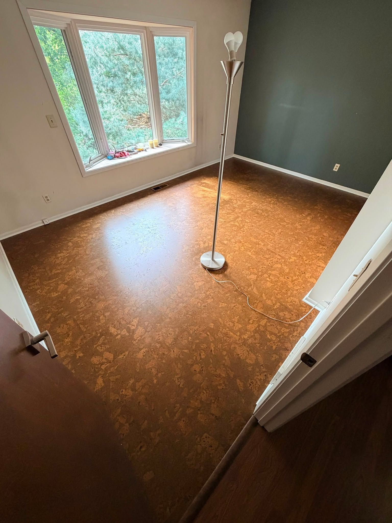 Cork tile flooring installed in bedroom with bay window and green accent wall.