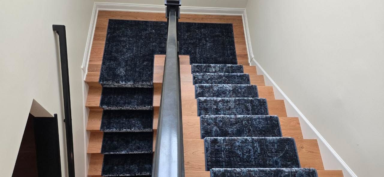 Staircase with black carpet runners installed on wooden steps and chrome metal rail.