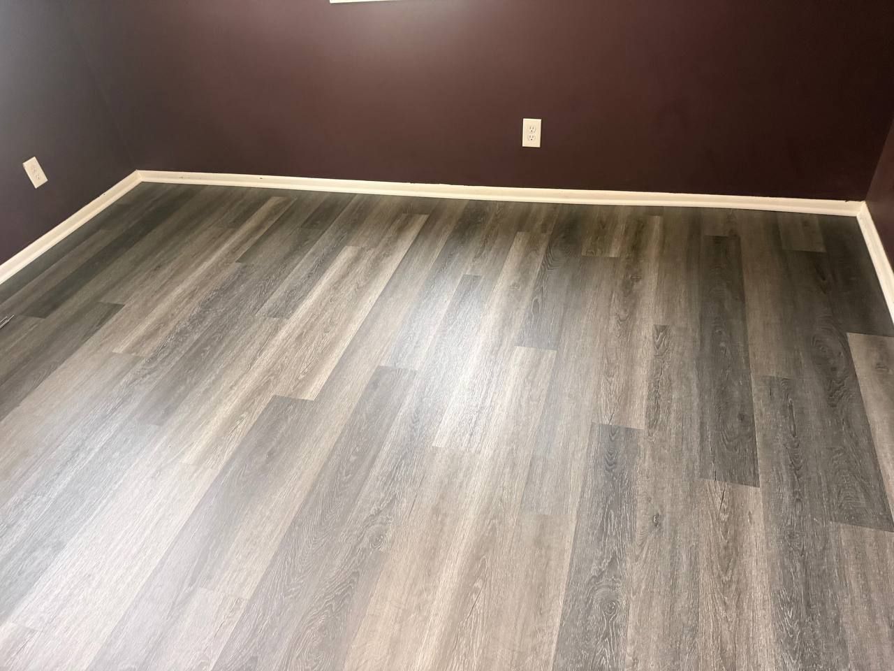 Newly installed gray and tan plank LVP flooring in a bedroom with white baseboard trim.