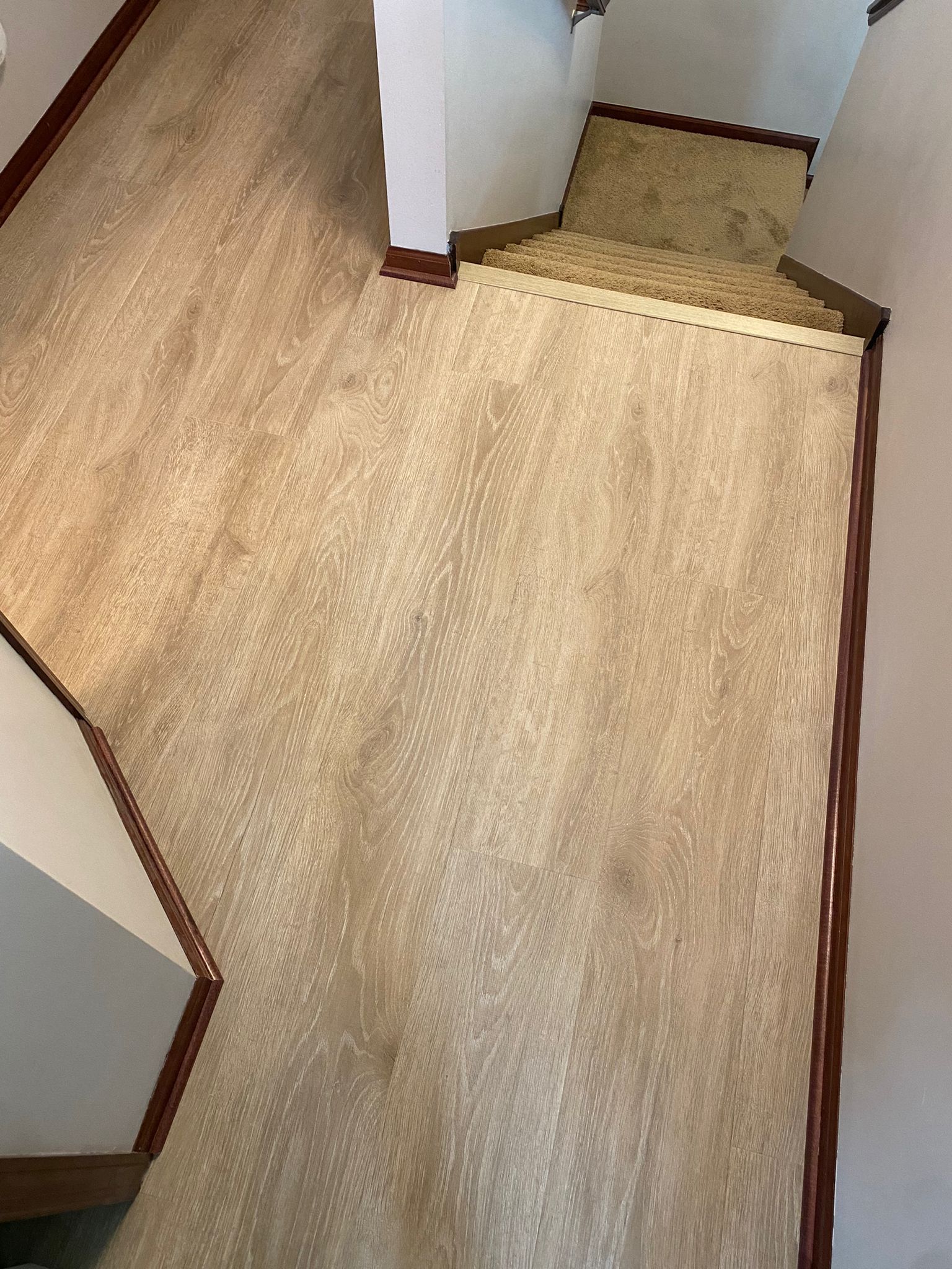 Hallway with light tan laminate plank flooring and dark brown trim transitioning to stairs.