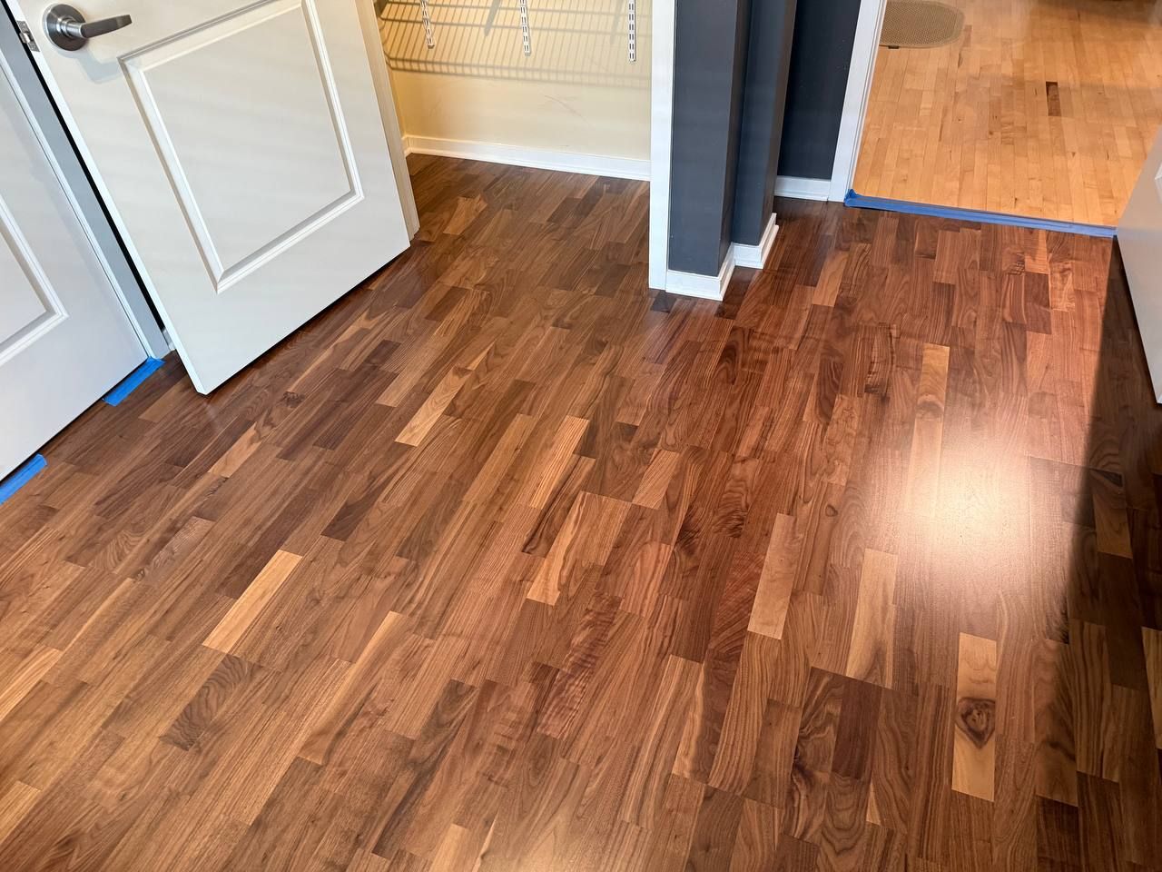 Newly installed medium brown hardwood plank flooring in an entryway with white trim and blue painter's tape on floor edges.