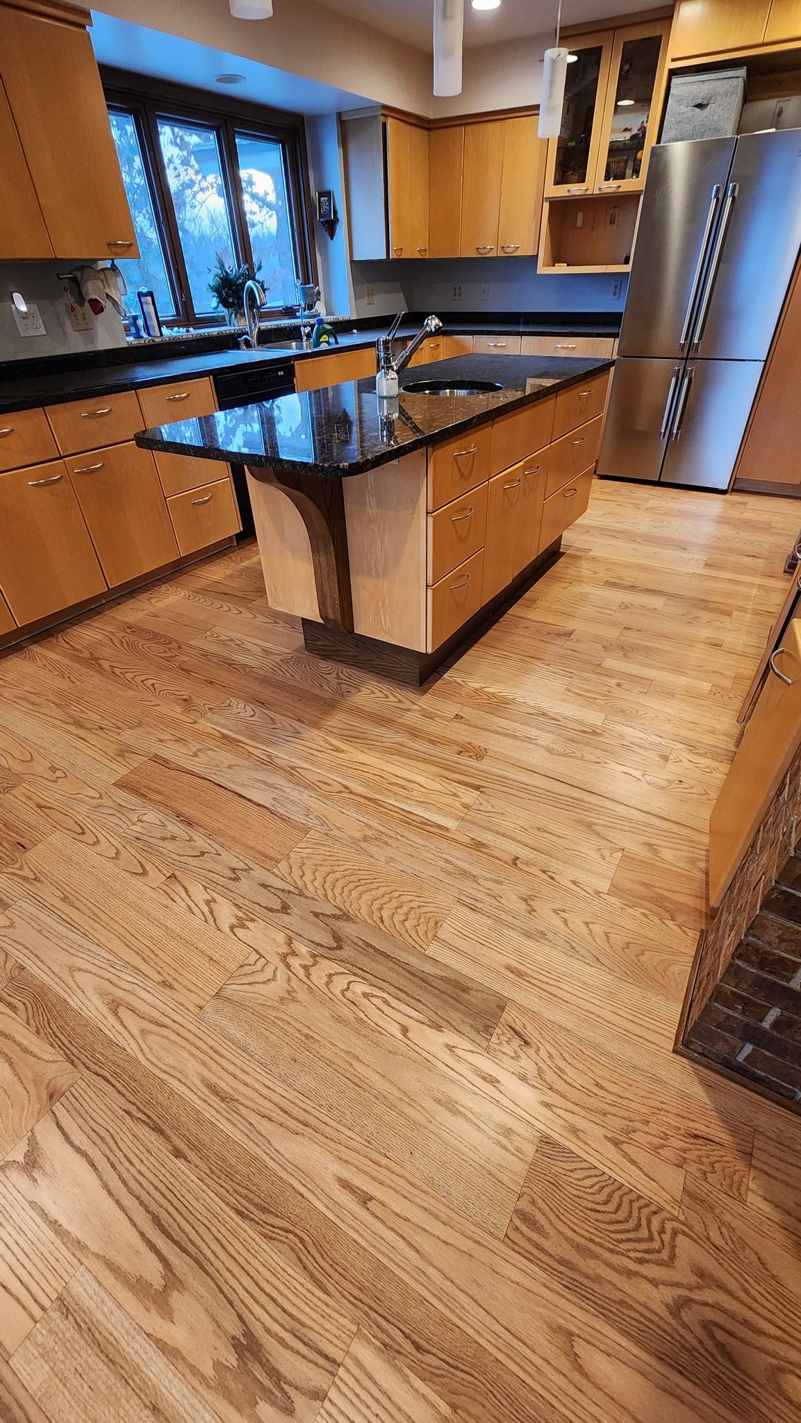 Red oak hardwood flooring installed throughout a kitchen with honey-toned cabinets and black granite countertops.