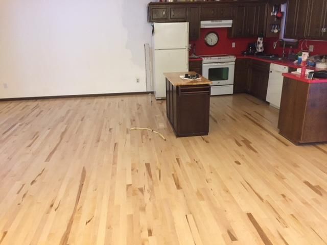 Light maple hardwood plank flooring in a kitchen with dark cabinets and red walls.