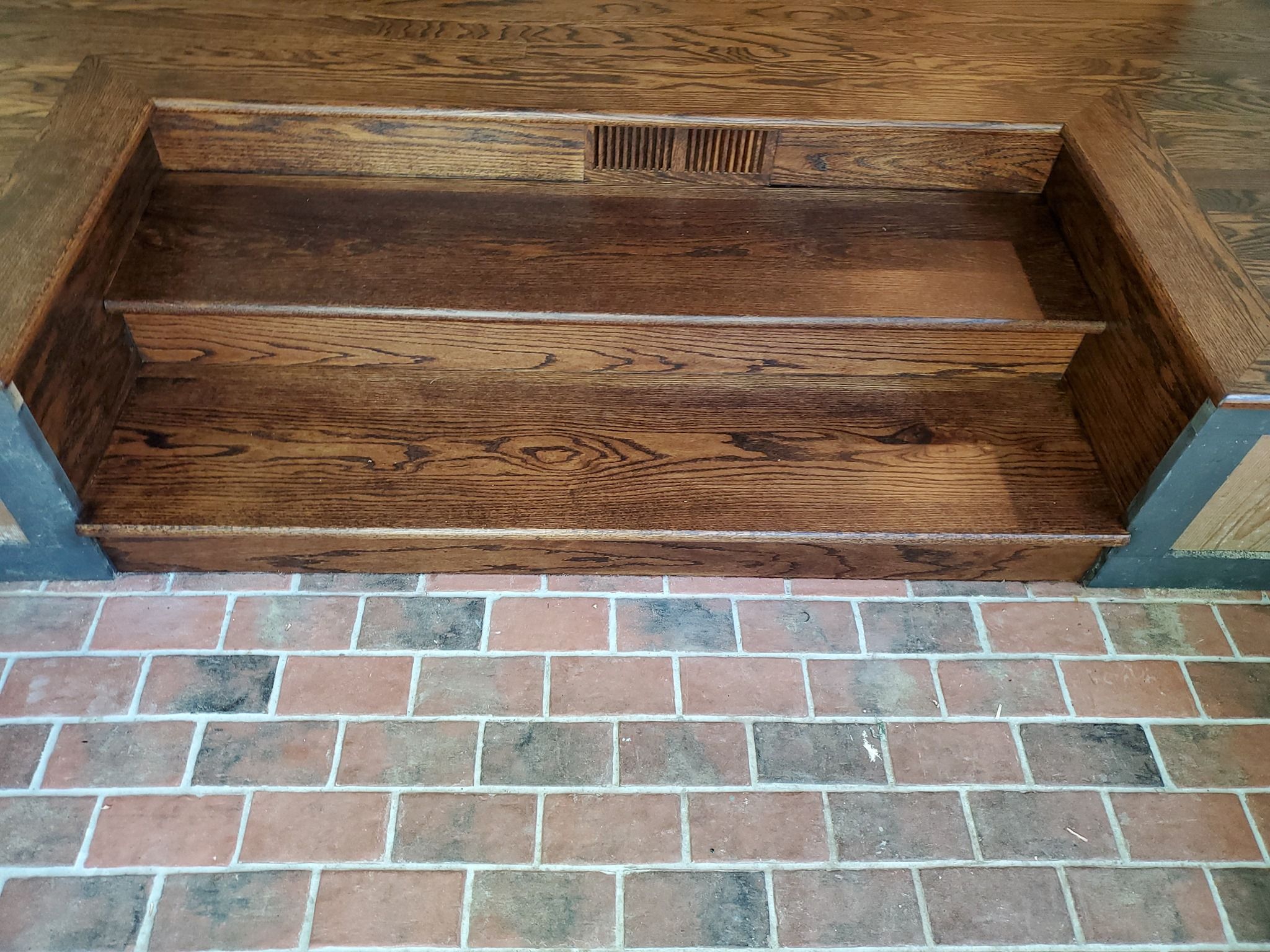Refinished red oak hardwood stair treads and landing with brick flooring visible below.