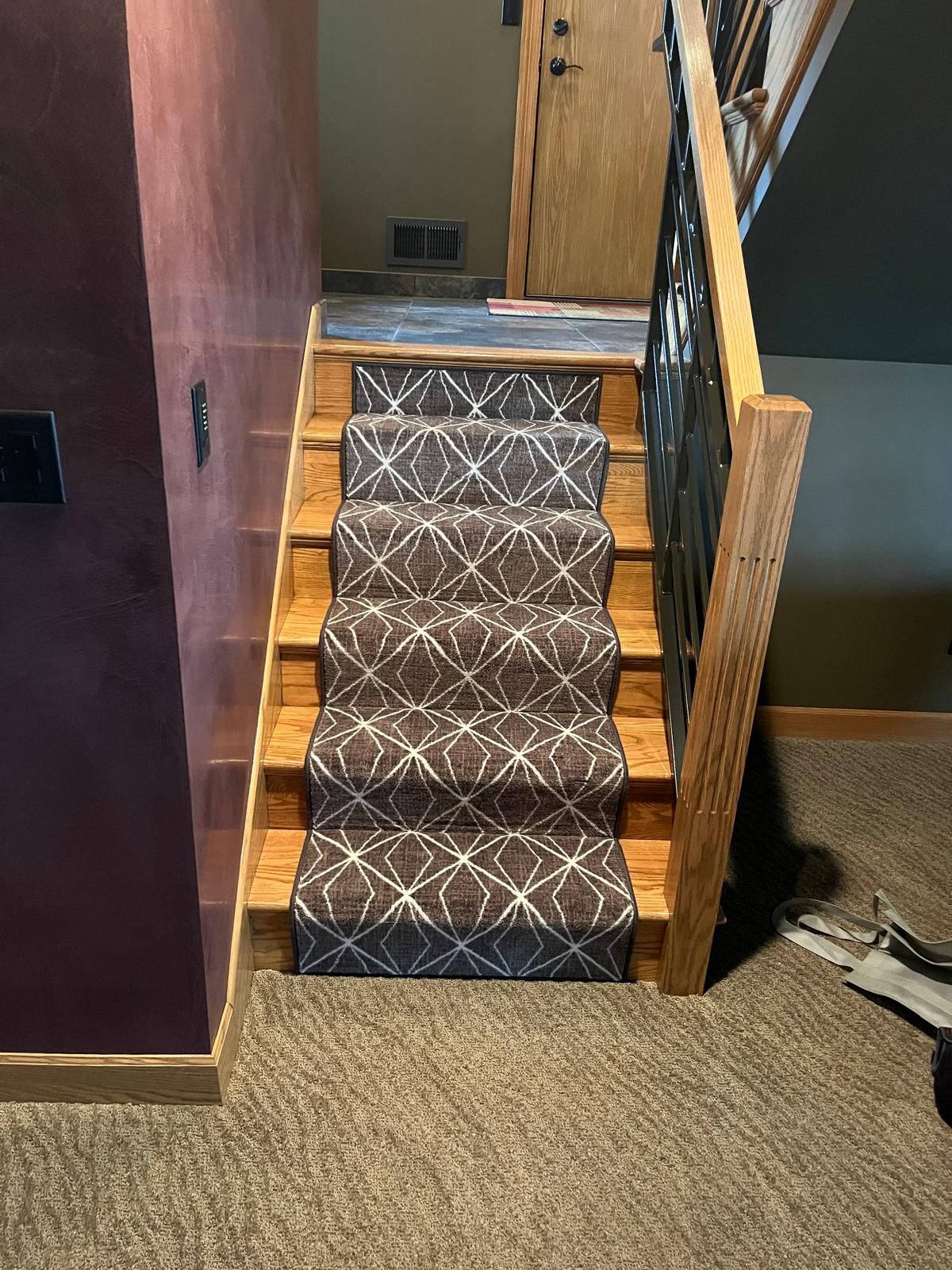 Staircase with geometric patterned carpet runner and wood railings connecting to hallway.