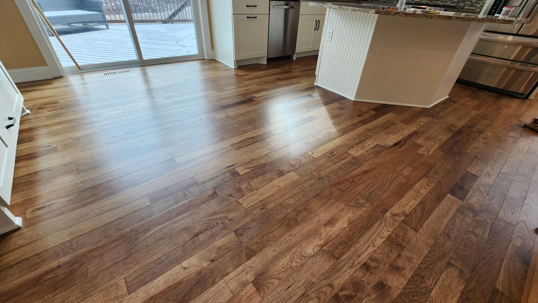 Refinished hickory hardwood plank flooring in a kitchen with island and large windows.