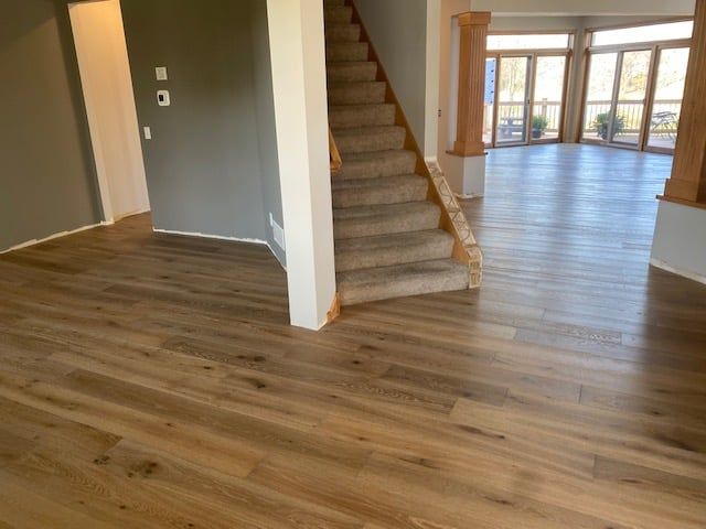 Engineered hardwood flooring in medium brown tones installed throughout an open hallway and living area with stairs visible.