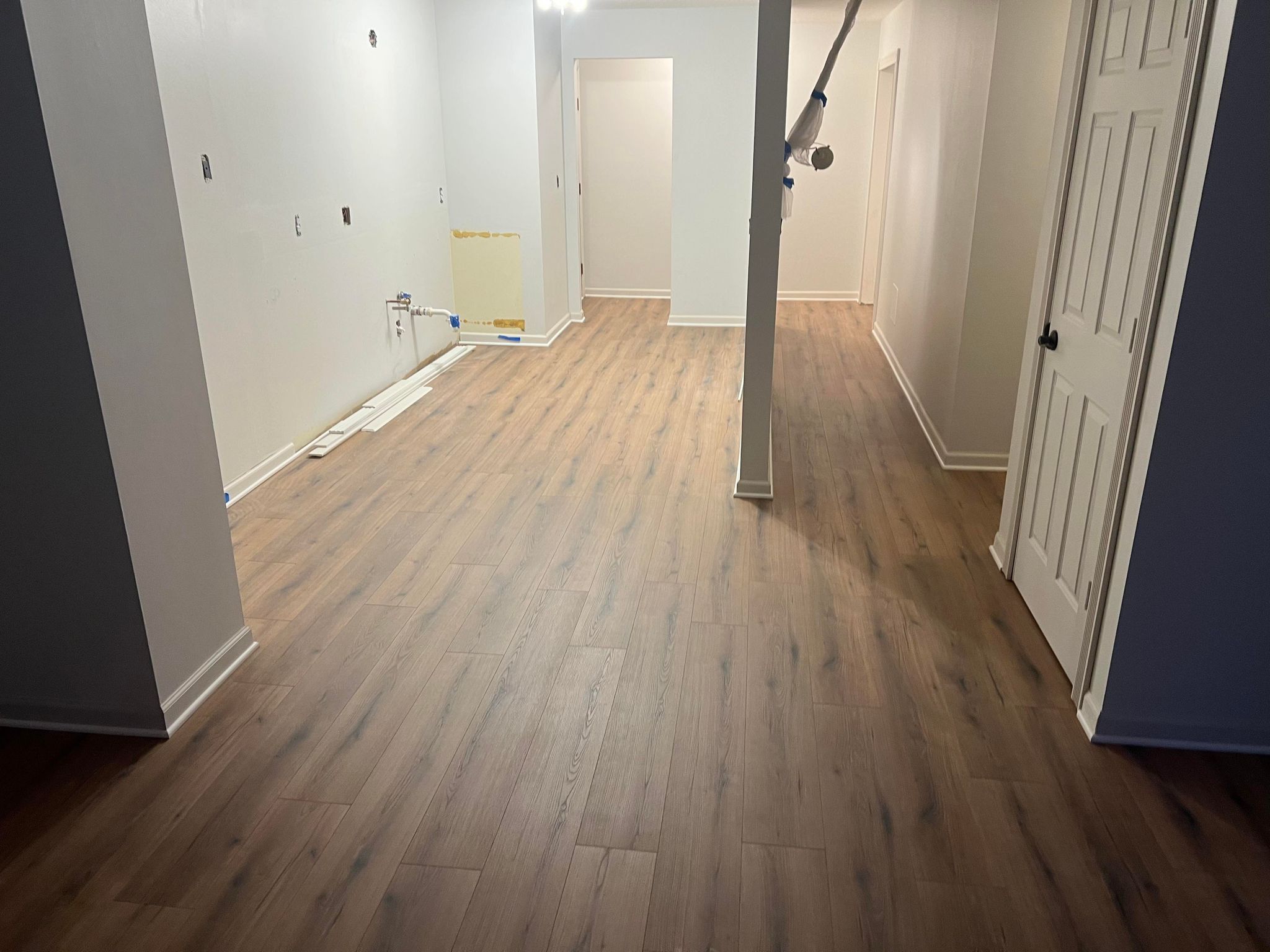 Newly installed laminate plank flooring in a hallway with white walls and closed doors.