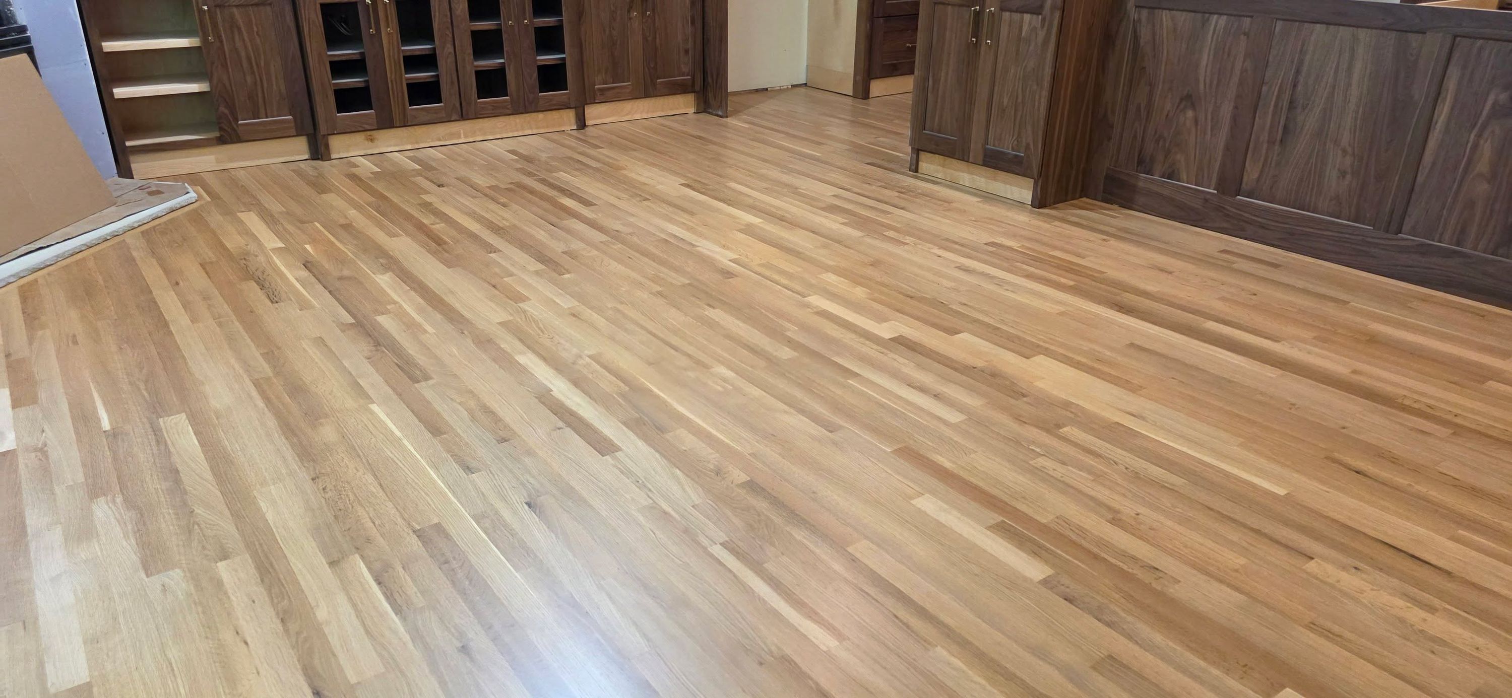 Newly refinished white oak hardwood plank flooring in a living room with built-in dark wood cabinetry.
