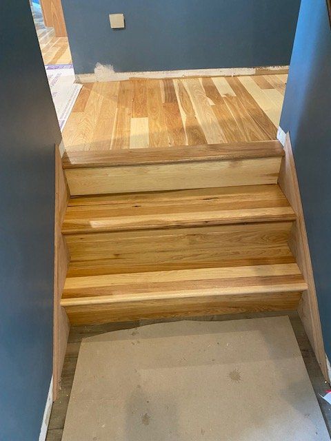 Hardwood stairs with mixed-tone planks during installation in a home with blue walls and adjacent hardwood flooring visible.