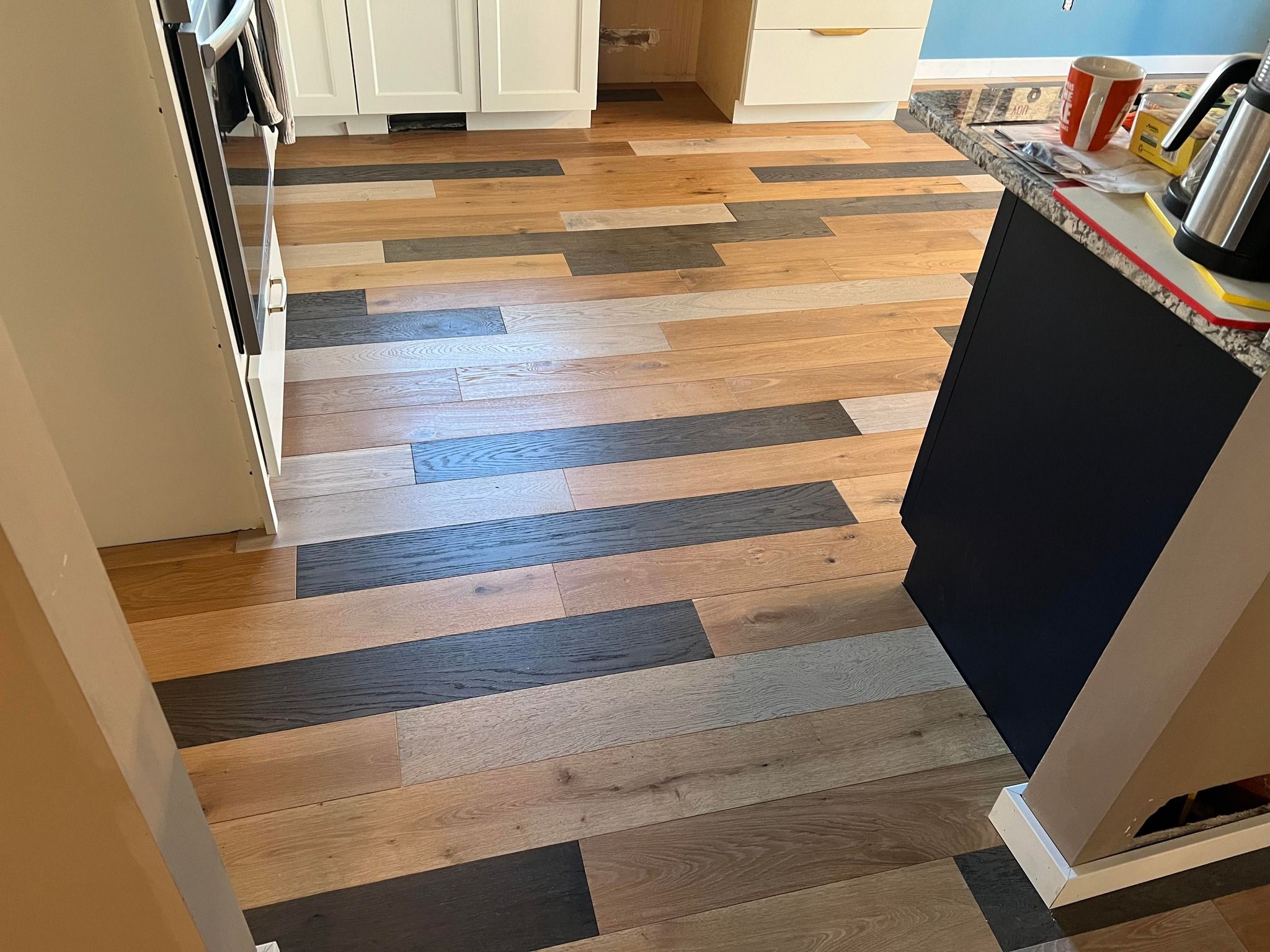 Kitchen hardwood flooring with mixed-width planks in varied tones arranged in a diagonal pattern.