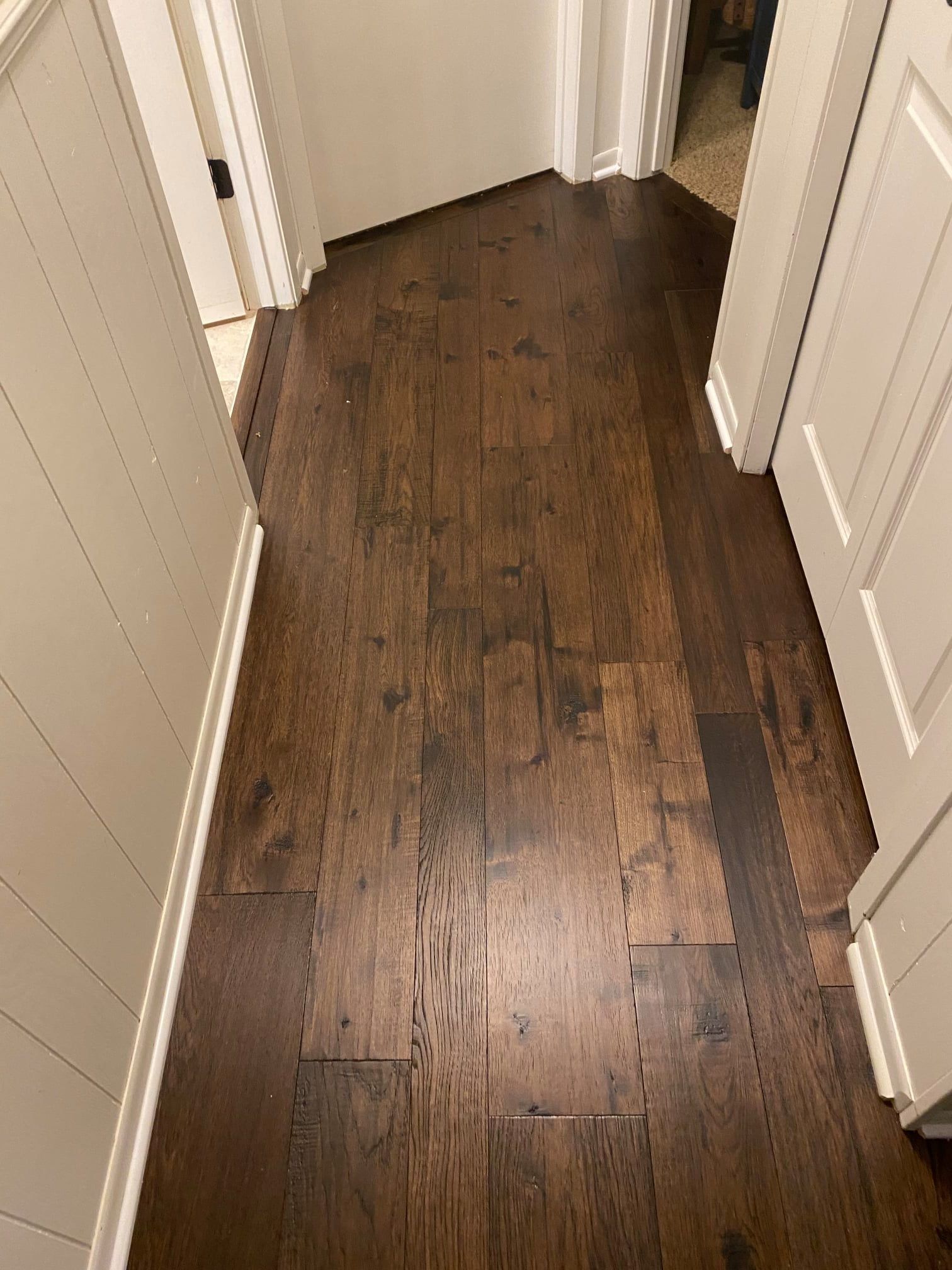 Dark brown hardwood plank flooring in a hallway with white trim and doors.