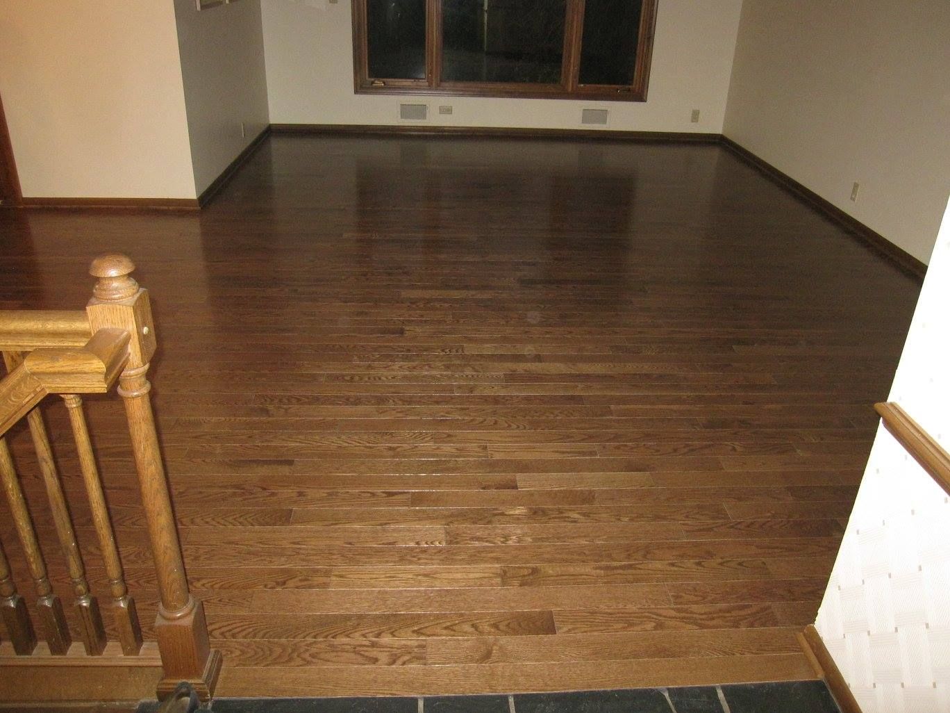 Medium-toned hardwood plank flooring in a hallway with wooden stair railing visible.
