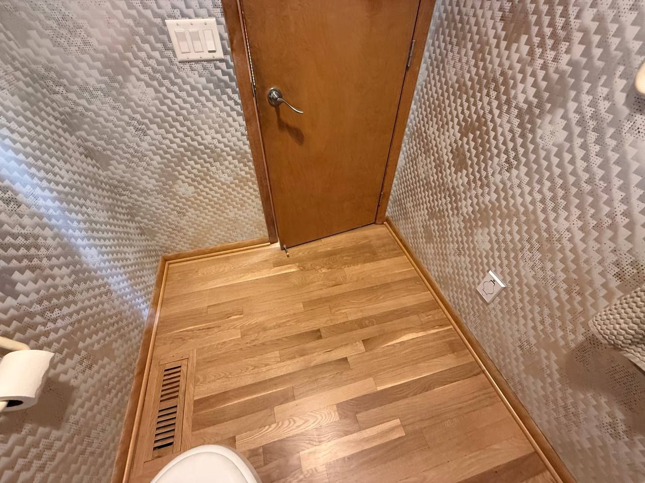 White oak hardwood flooring installed in bathroom with random width planks and matching wood trim around door frame.