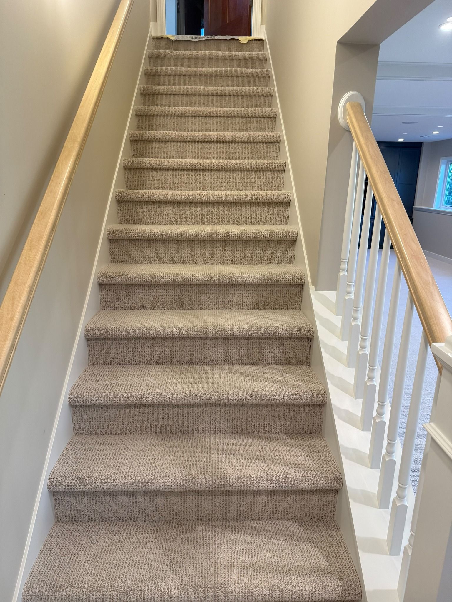 Beige textured carpet installed on staircase with wooden handrail and white spindle railings.