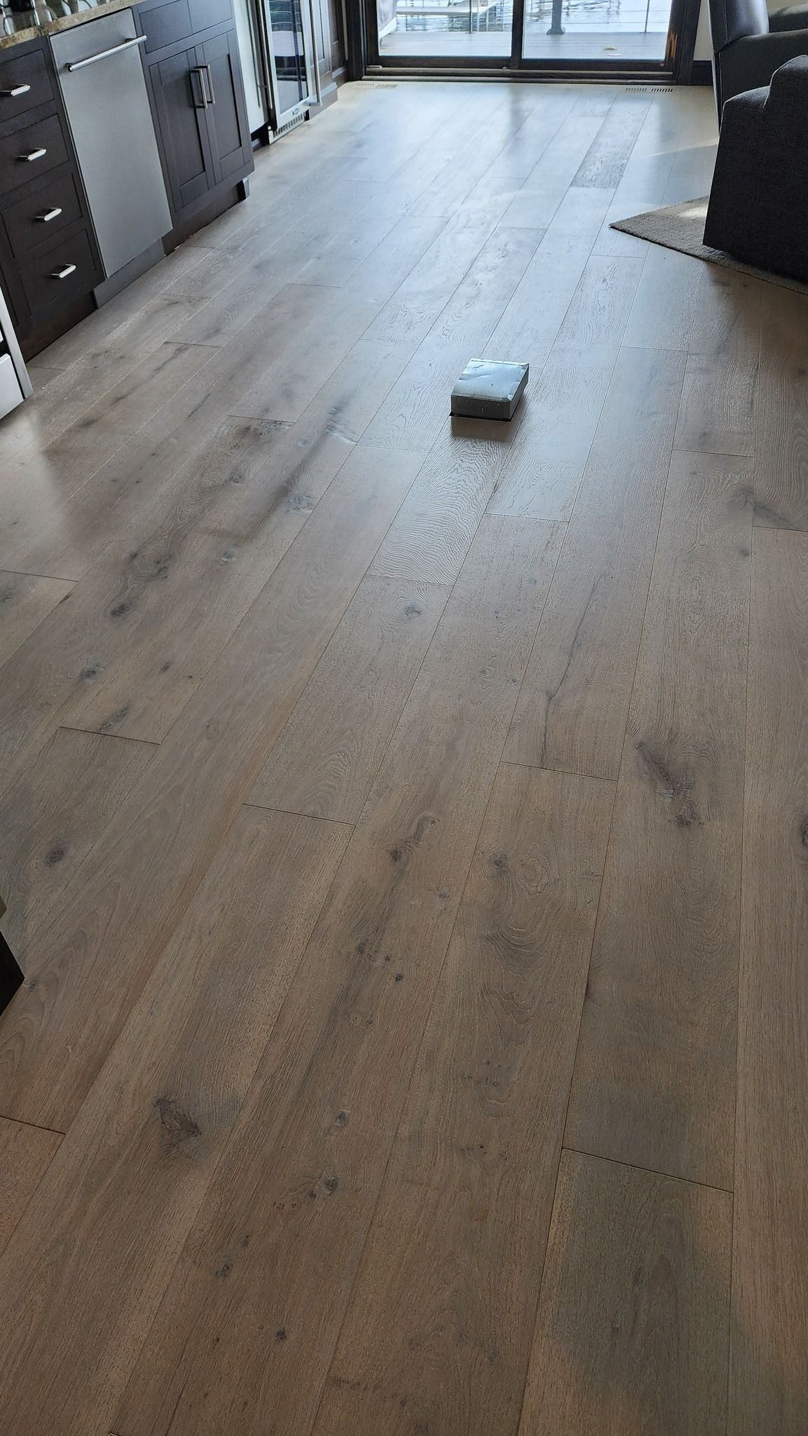 Light gray and tan hardwood plank flooring in a kitchen with dark cabinetry and stainless steel appliances.