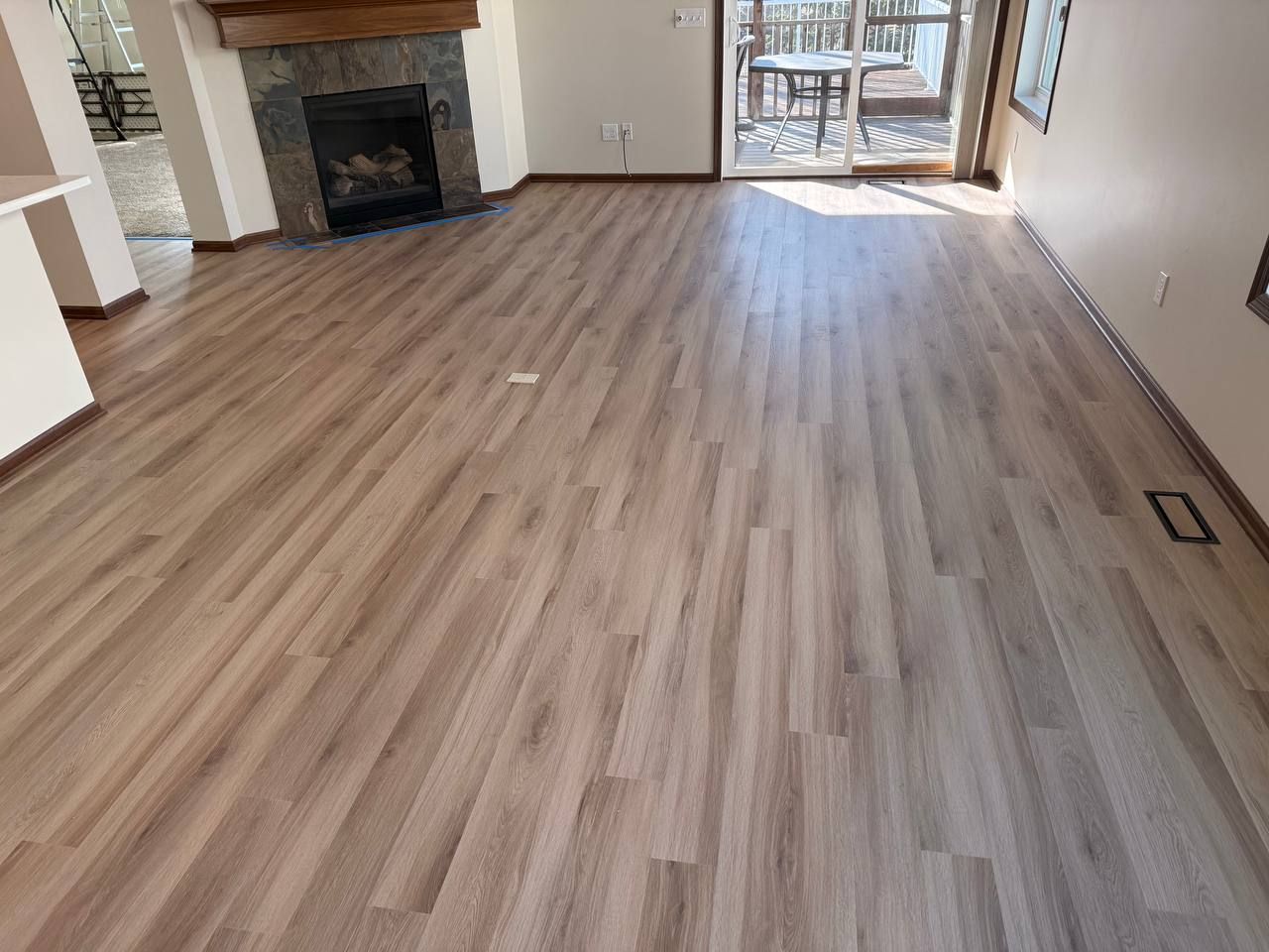 Light tan and gray plank LVP flooring installed in a living room with fireplace and glass doors to deck.