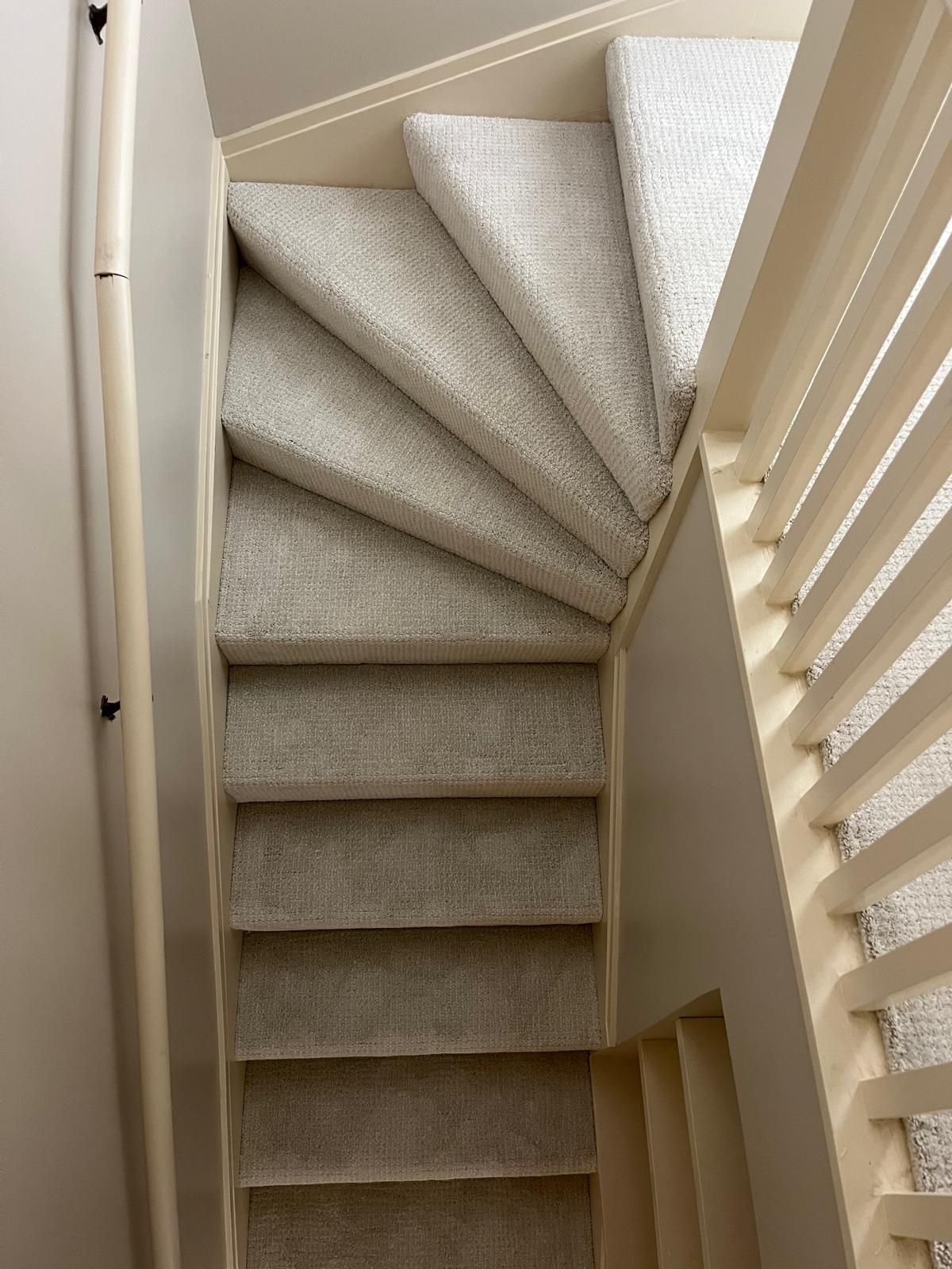 Carpeted staircase with light beige textured carpet and white trim in a residential stairwell.