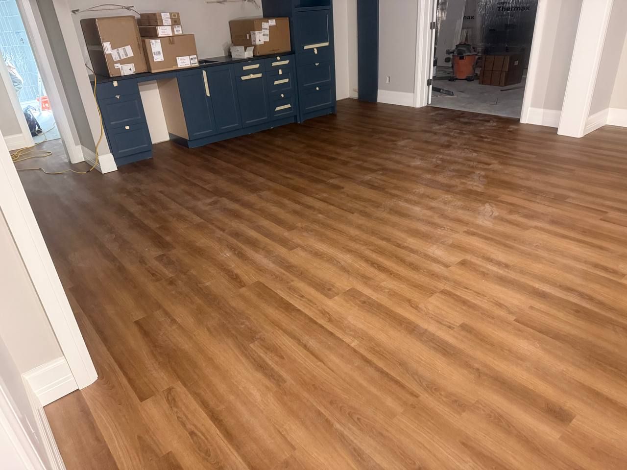 Glued down luxury vinyl plank flooring in medium brown wood tone installed in a living space with navy cabinetry.