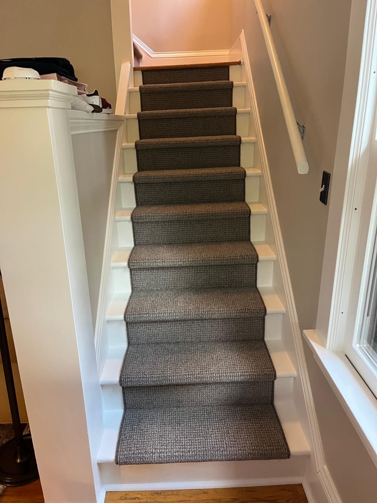 Gray textured carpet runner installed on basement stairs with white risers and natural wood handrails.