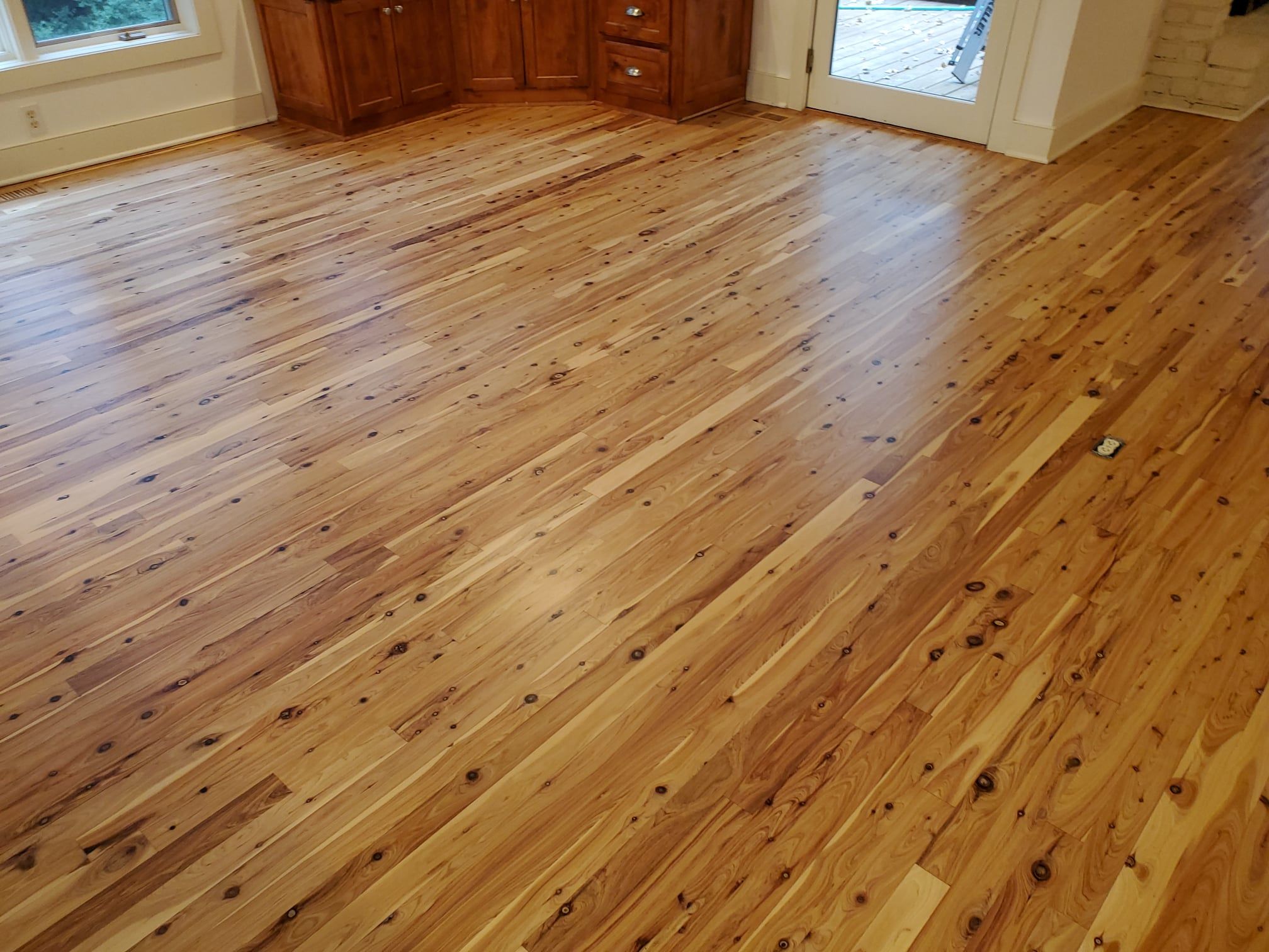 Refinished knotty hardwood plank flooring with golden-amber finish in a bright room with wood cabinetry.