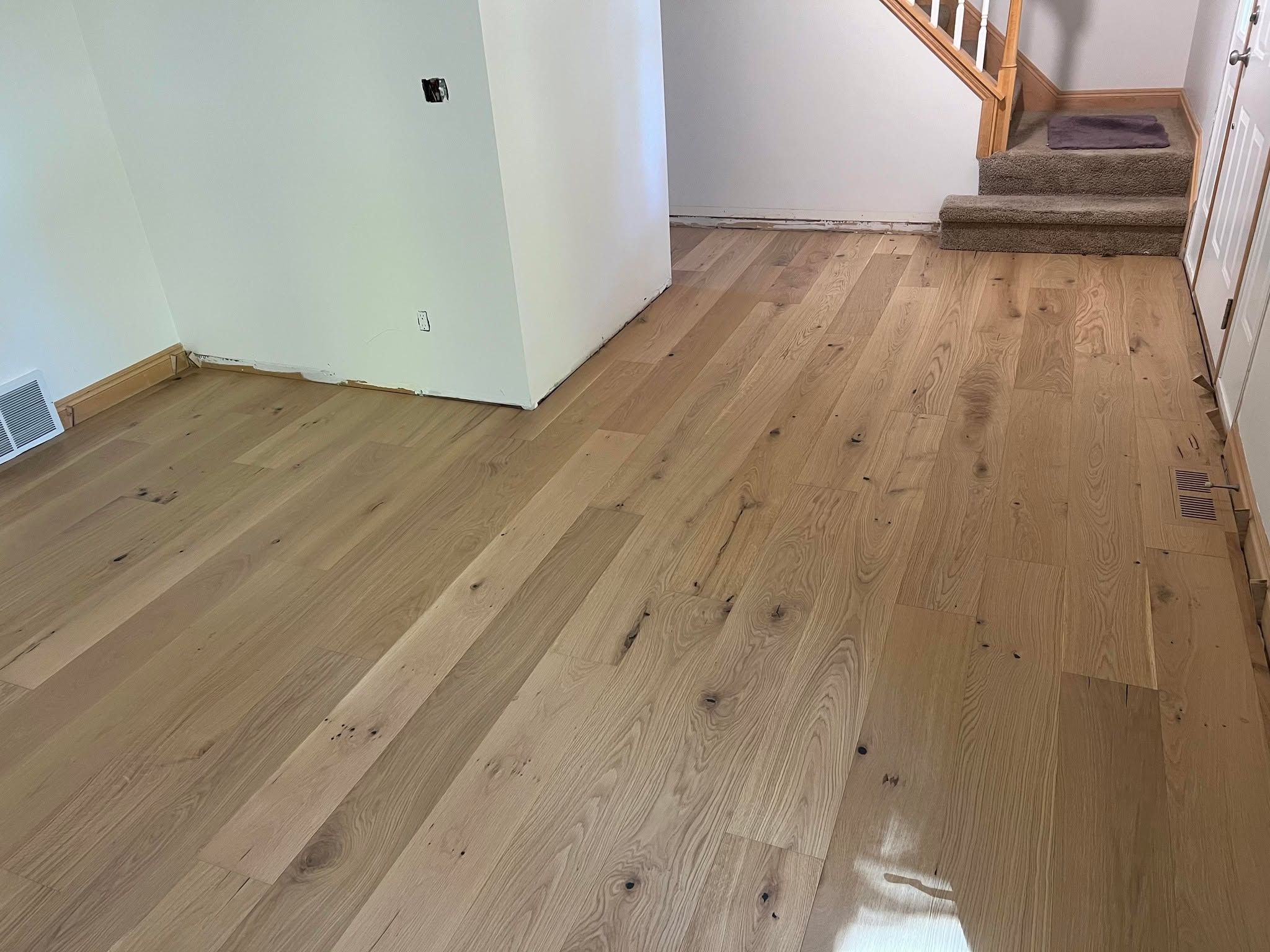 Light tan and brown hardwood plank flooring installed in a hallway leading to stairs.