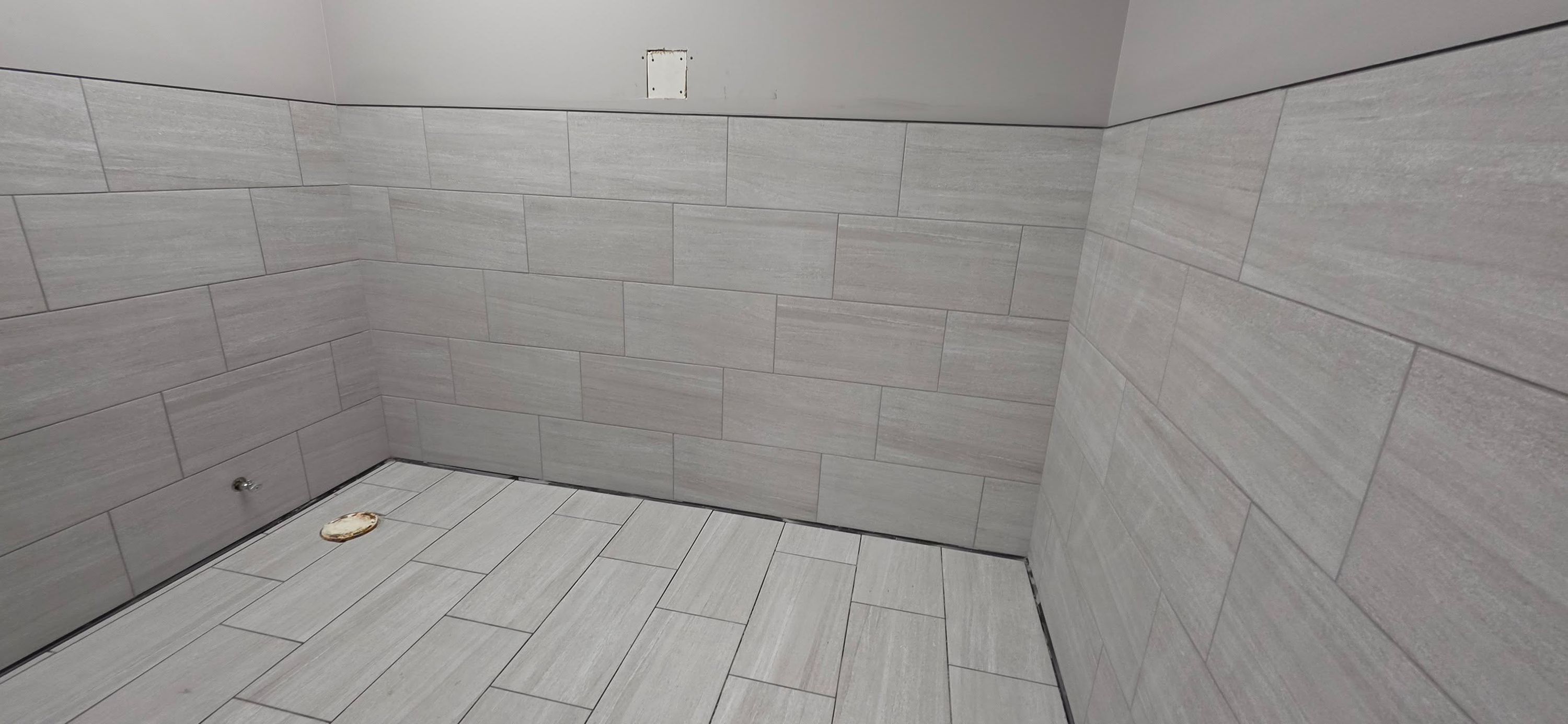 Empty bathroom with gray subway tile walls and light plank-pattern tile flooring.