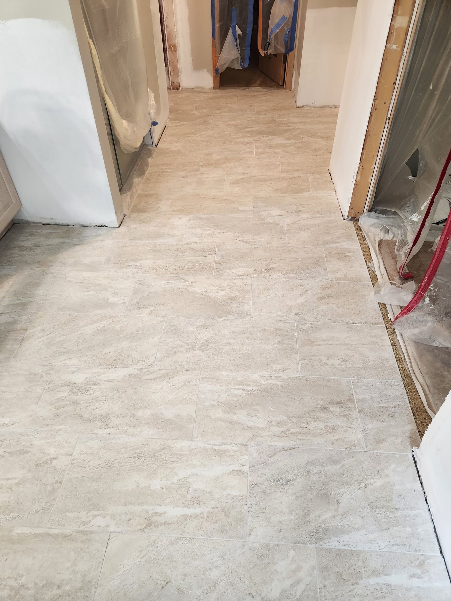 Hallway with light beige plank-style tile flooring during installation.