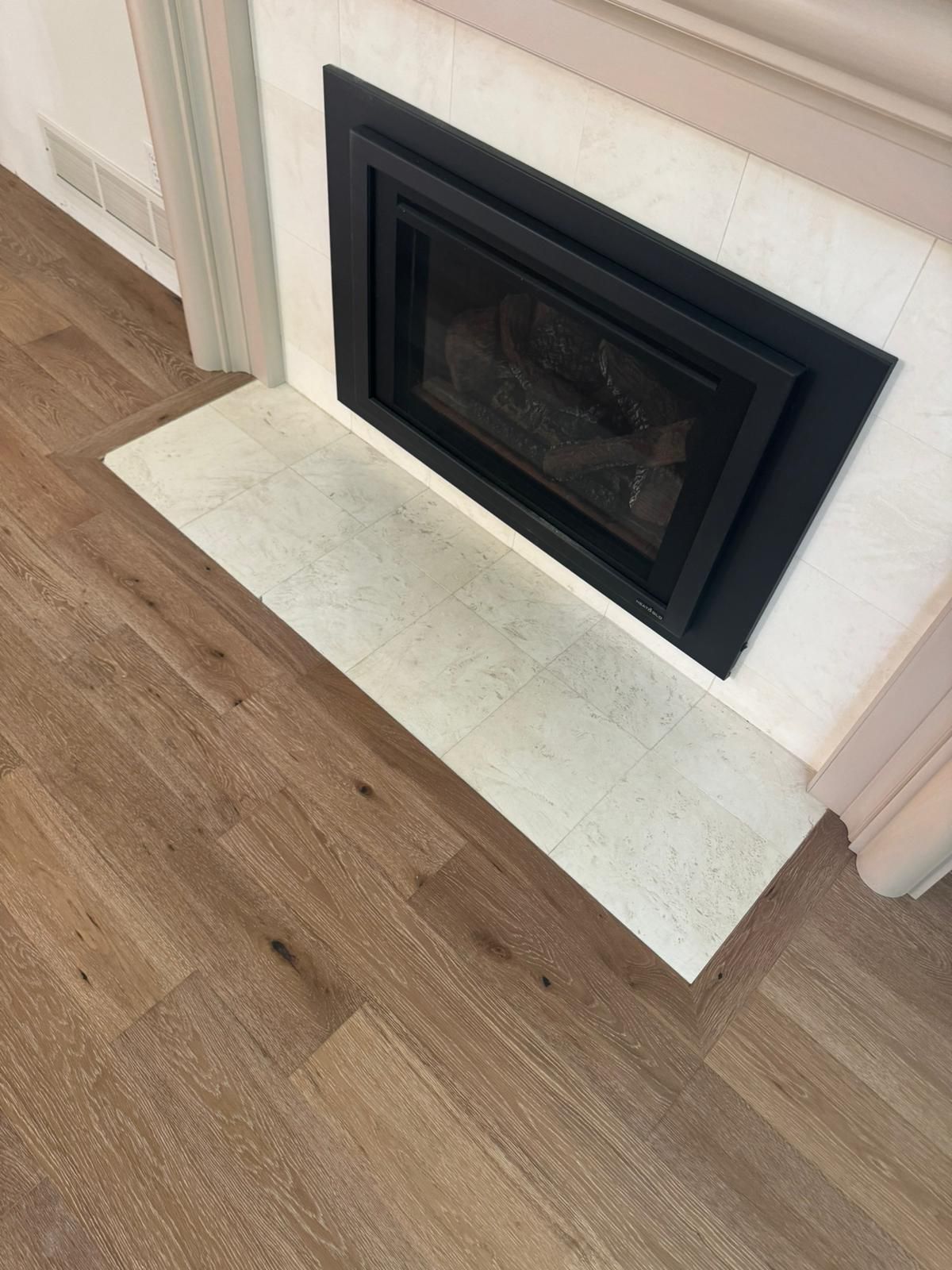 Hardwood flooring in herringbone pattern adjacent to fireplace with white tile hearth.